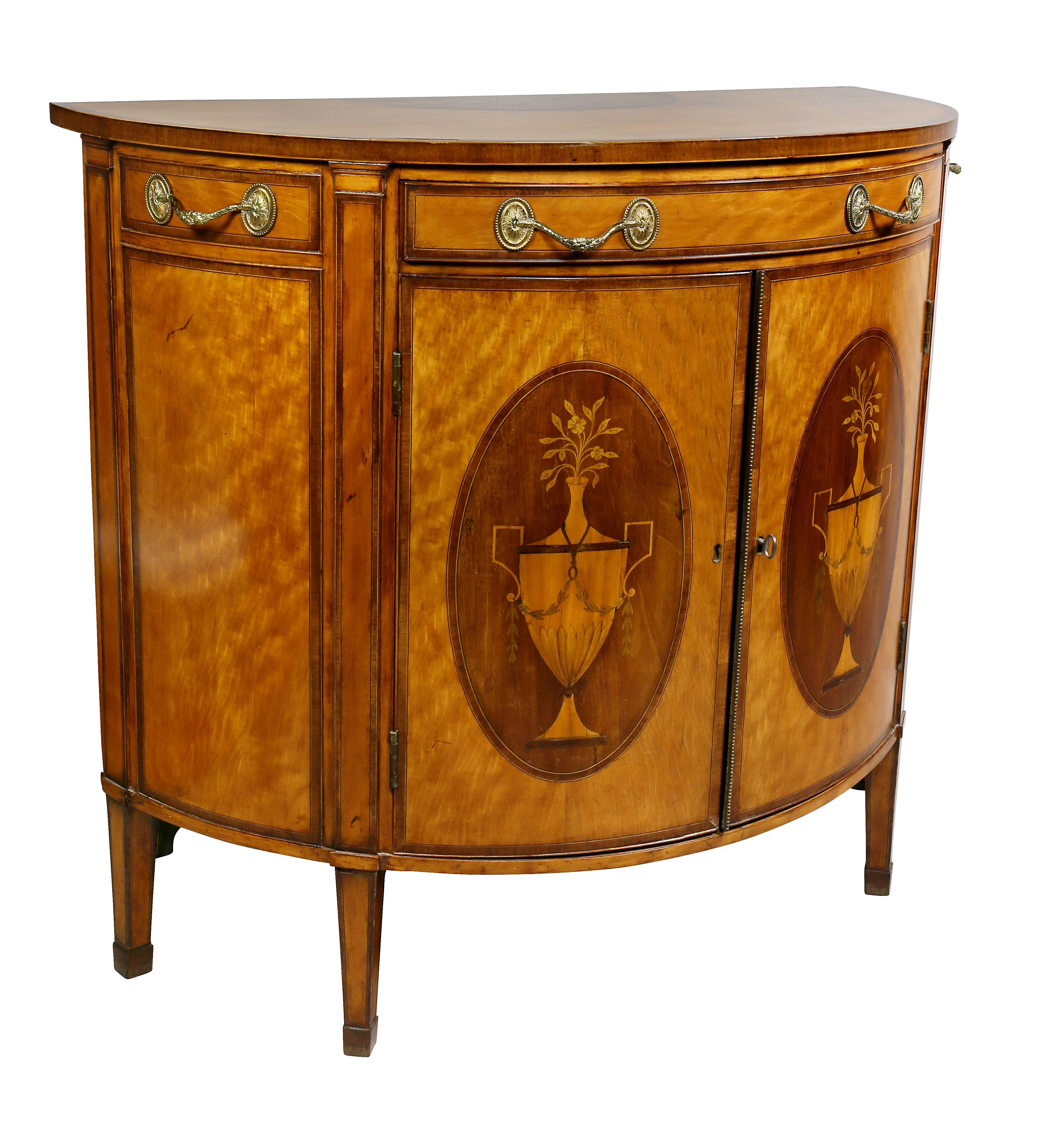 With cross banded top with inlaid lunette over a drawer with fire gilt handles and a pair of doors with inlaid urns within an oval panel enclosing two shelves raised on square tapered legs. Back boards replaced. Written on inside edge of door frame