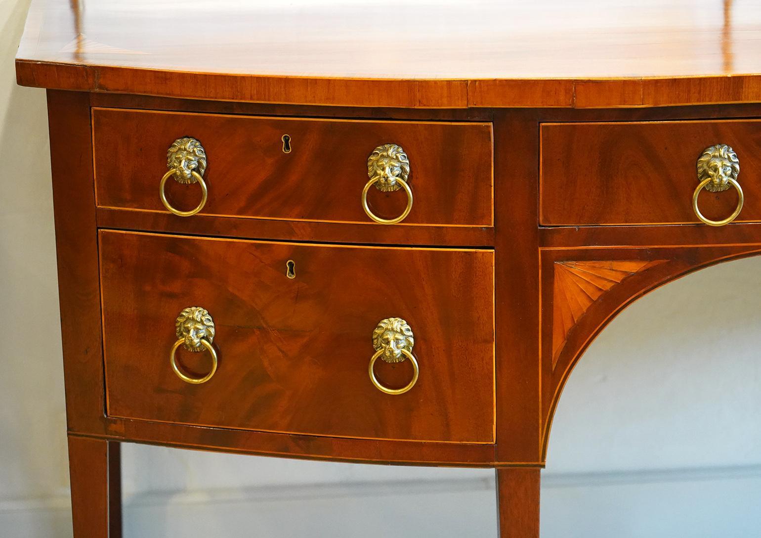 This George III bowfront sideboard features a polished banded one plank top with double brass rail along the back. The front has a center drawer flanked by two drawers to the left and one deep drawer to the right looking like two drawers. All