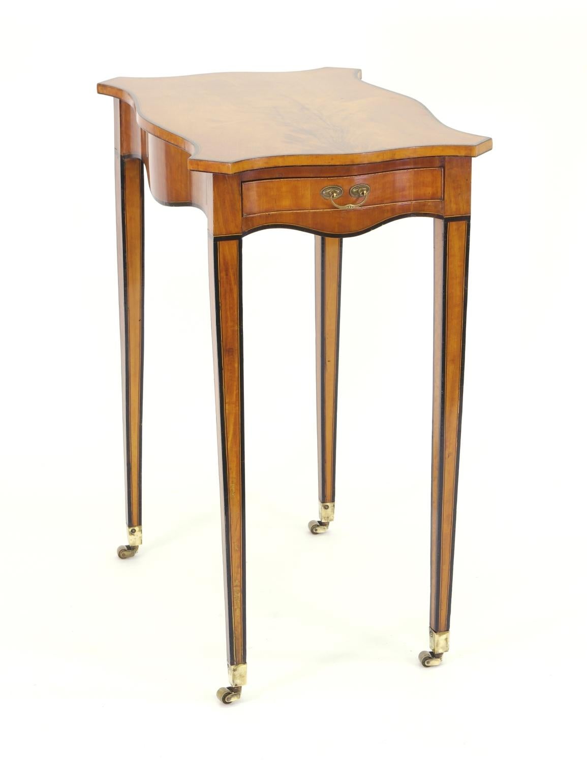 George III satinwood side table, the serpentine top with beautifully figured veneer and ebony banded edge over the conforming apron with a single drawer; the square tapering banded legs ending with brass casters.