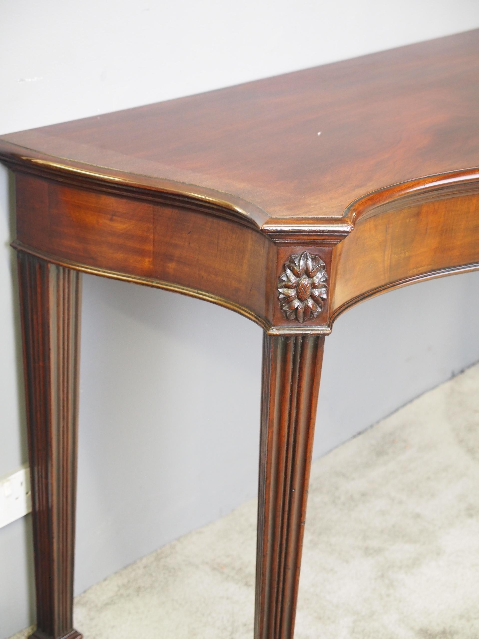 George III serpentine front mahogany hall or serving table, c irca 1780. The shaped top in rich figured Spanish mahogany with a molded fore-edge over a cross-banded frieze. There are canted corners with carved oval paterae over square, fluted,