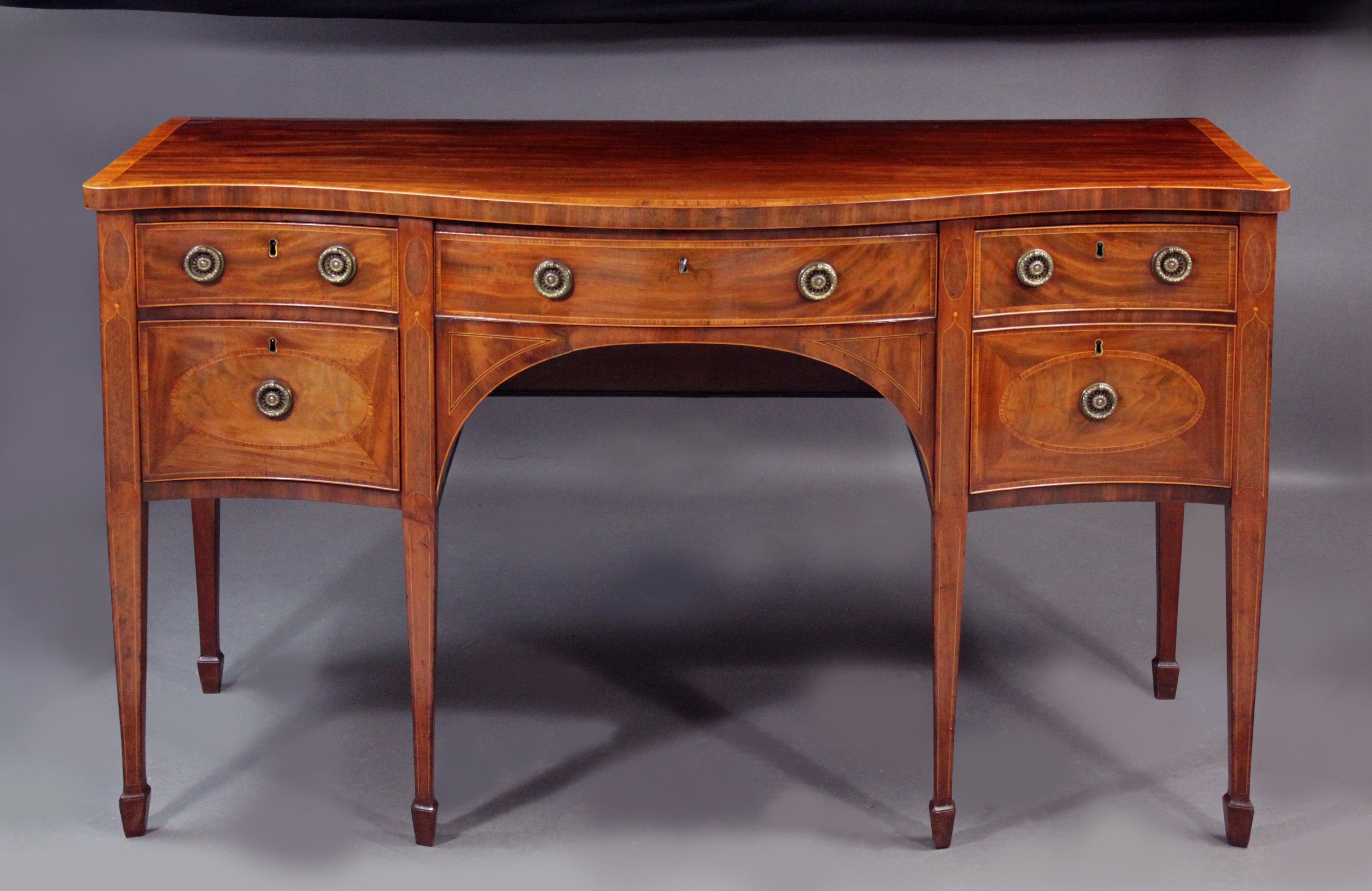 A fine quality George III serpentine sideboard in the manner of Thomas Sheraton: figured mahogany with tulip wood cross-banding and attractive inlays including ovals to the lower drawers and boxwood cock-beading which extend to the depth of the