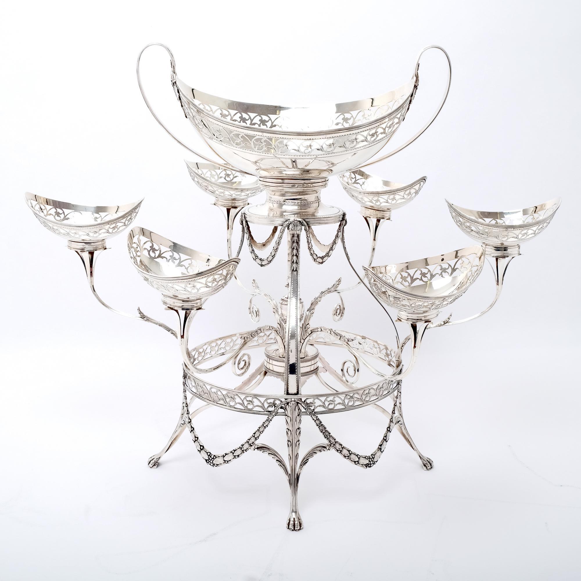 An elegant Georgian neoclassical sterling silver épergne with seven baskets. The oval frame has bands of pierced and engraved decoration and is supported on four acanthus leaf legs with lion's paw feet with acanthus leaf garlands between. It has six