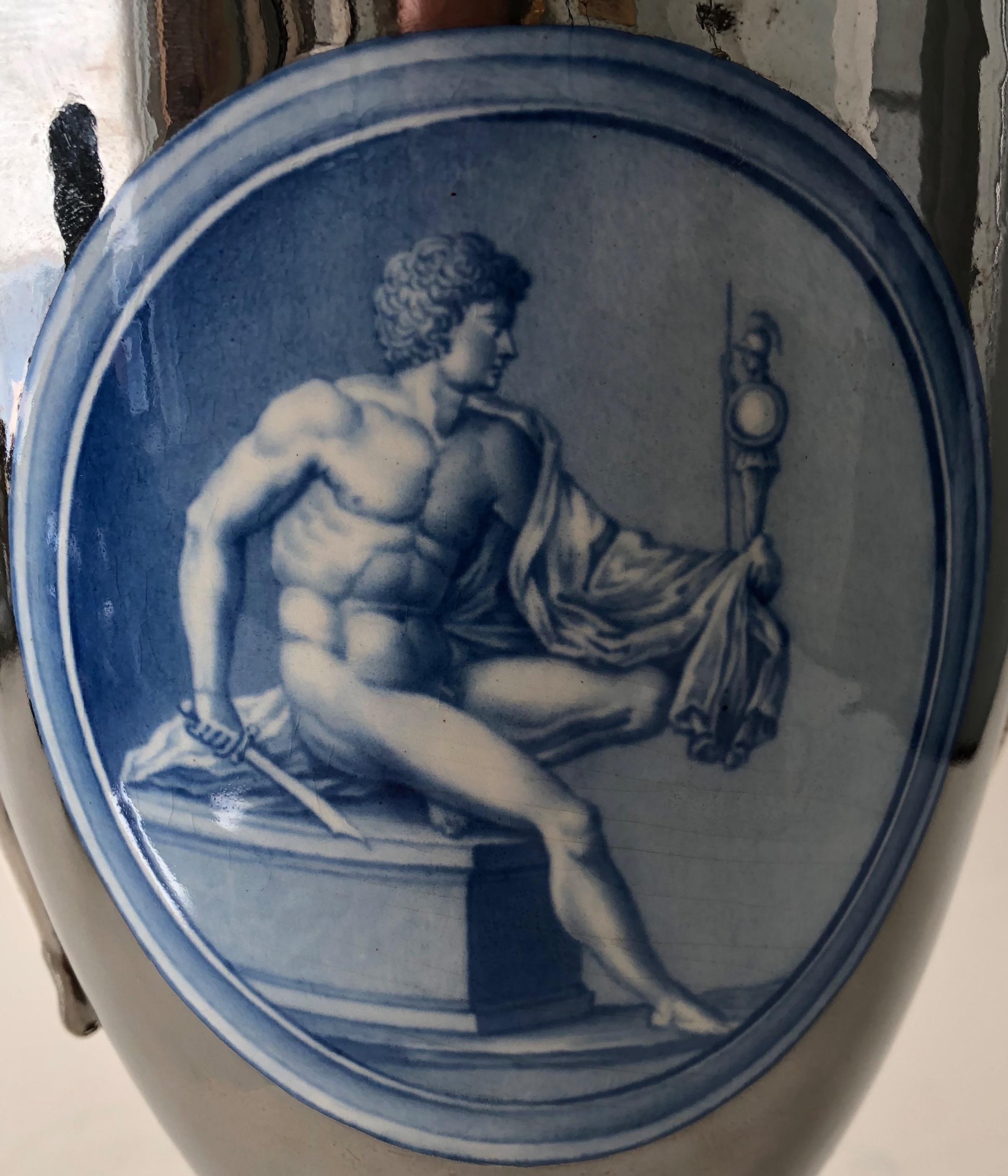 This elegant vase of attenuated proportions was given an unusual silver-luster glaze, and embellished with two medallions on a military theme. One depicts a young soldier with a sword and statuette of Athena, goddess of war. The other an older,
