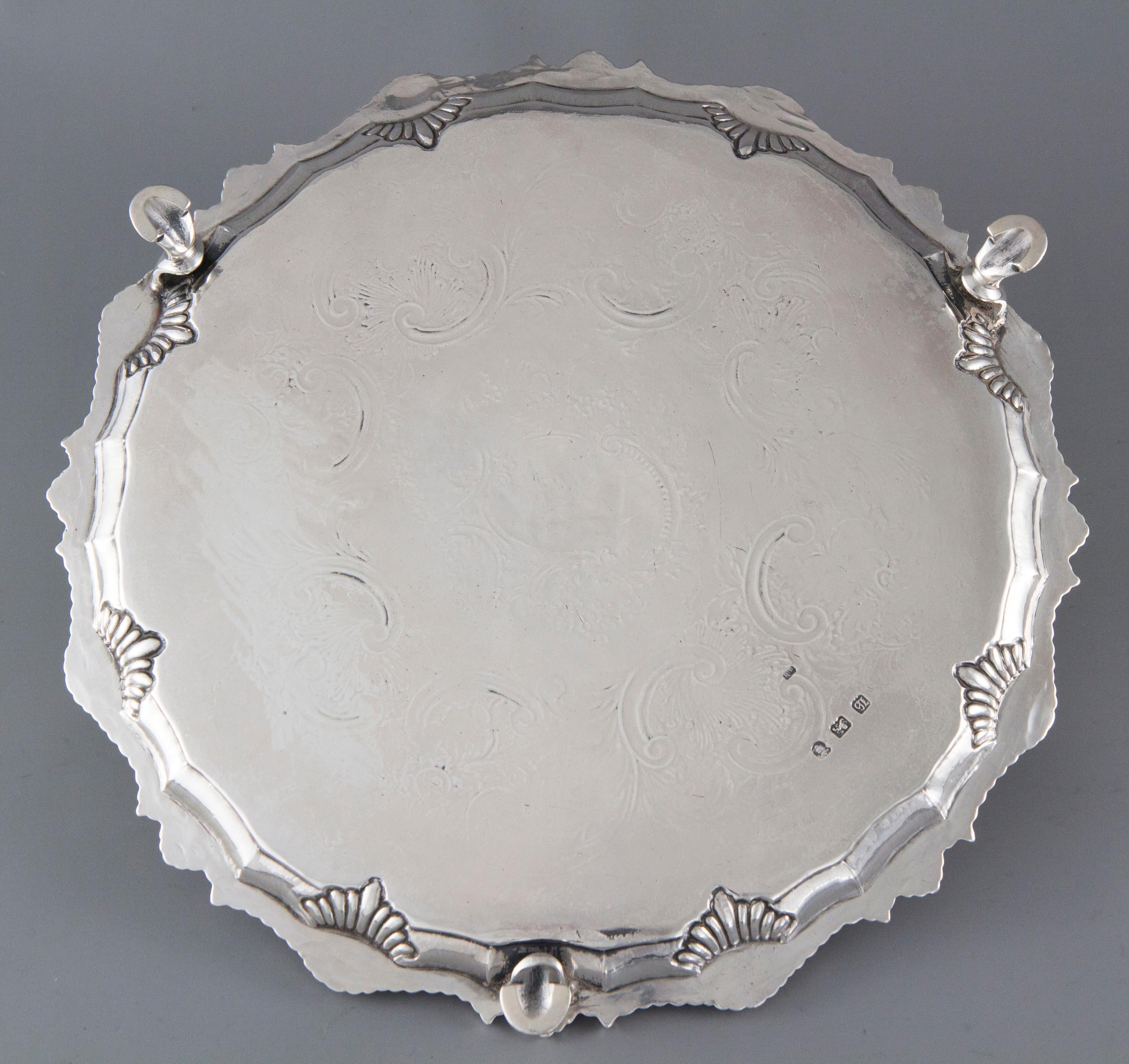 A very good quality silver salver of circular form. The plate engraved with floral and foliate arabesques about a vacant shaped cartouche. The cast rim of fluted shell form decoration. The whole standing on three cast C-scroll hoof feet.

Clearly