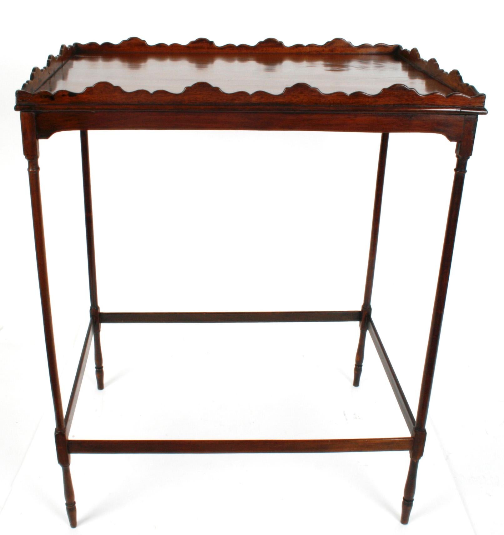 A George III Mahogany silver/tea table, c1780. The table base has four finely turned (spider) legs with cross stretchers and blocks at the joints. The table has an oblong, single board, mahogany top with a fancy scalloped gallery. Although the table