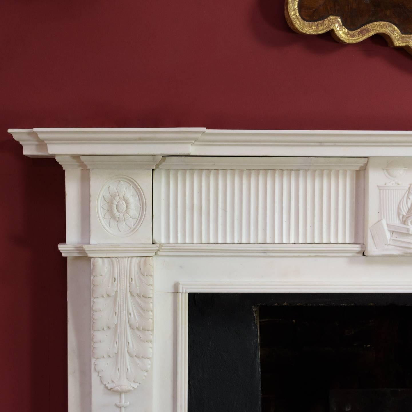 George III statuary marble chimneypiece, circa 1780, the inverse breakfront shelf above fluted frieze flanked by oval paterae end blocks and centered with tablet depicting Urania (Muse of Astronomy), the pilaster jambs with acanthus volutes hung
