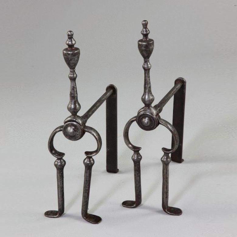 An antique pair of George III steel fire dogs. 

These steel fire dogs have front supports shaped like short tongs with urn and baluster finials.