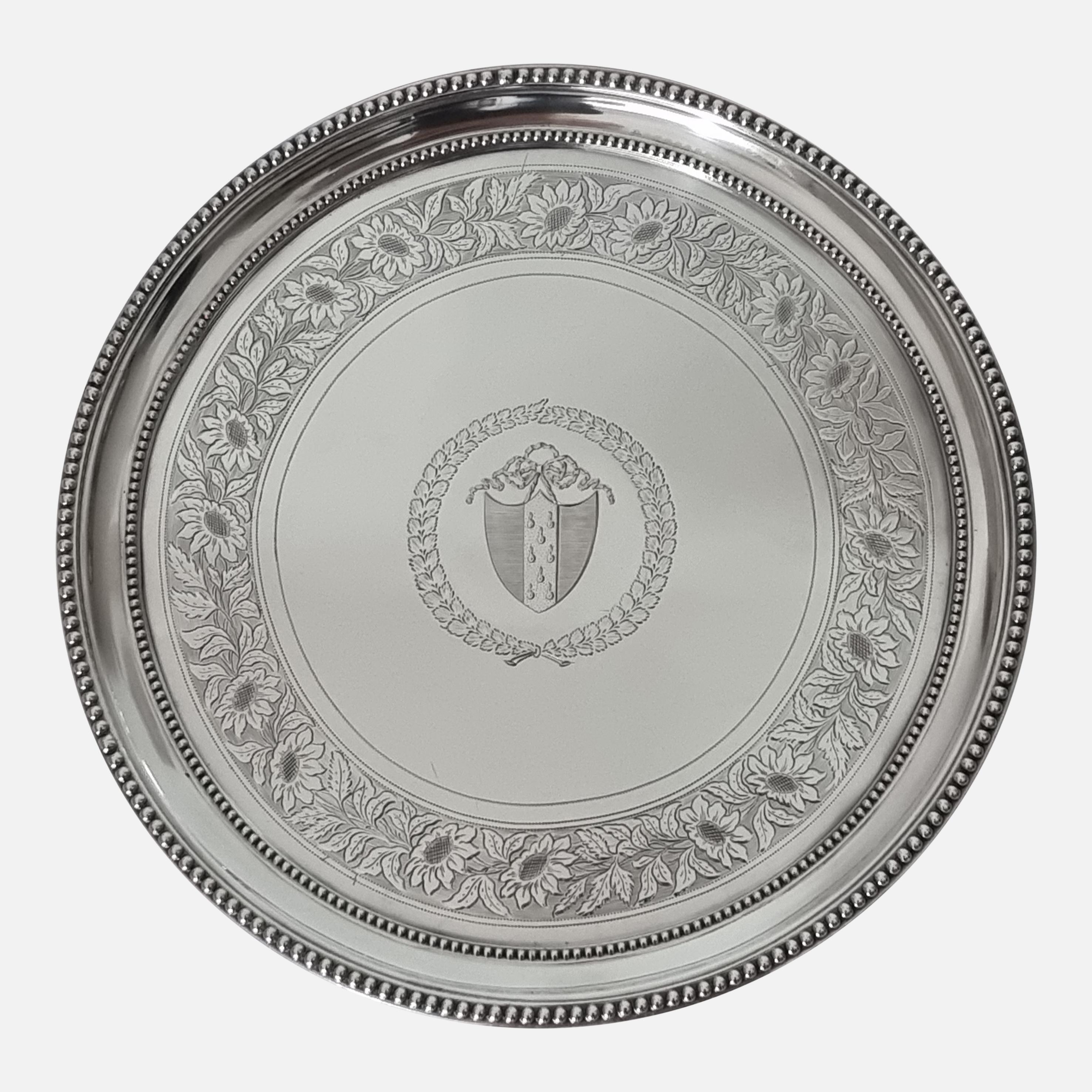 Bandeja de plata de ley de Jorge III de 1814, obra de William Bennett, adornada con bordes de cuentas y decoración foliada cincelada, con un escudo de armas dentro de un manto foliado, asentada sobre tres patas acanaladas.

- Medidas: 28,2 cm (Dia)