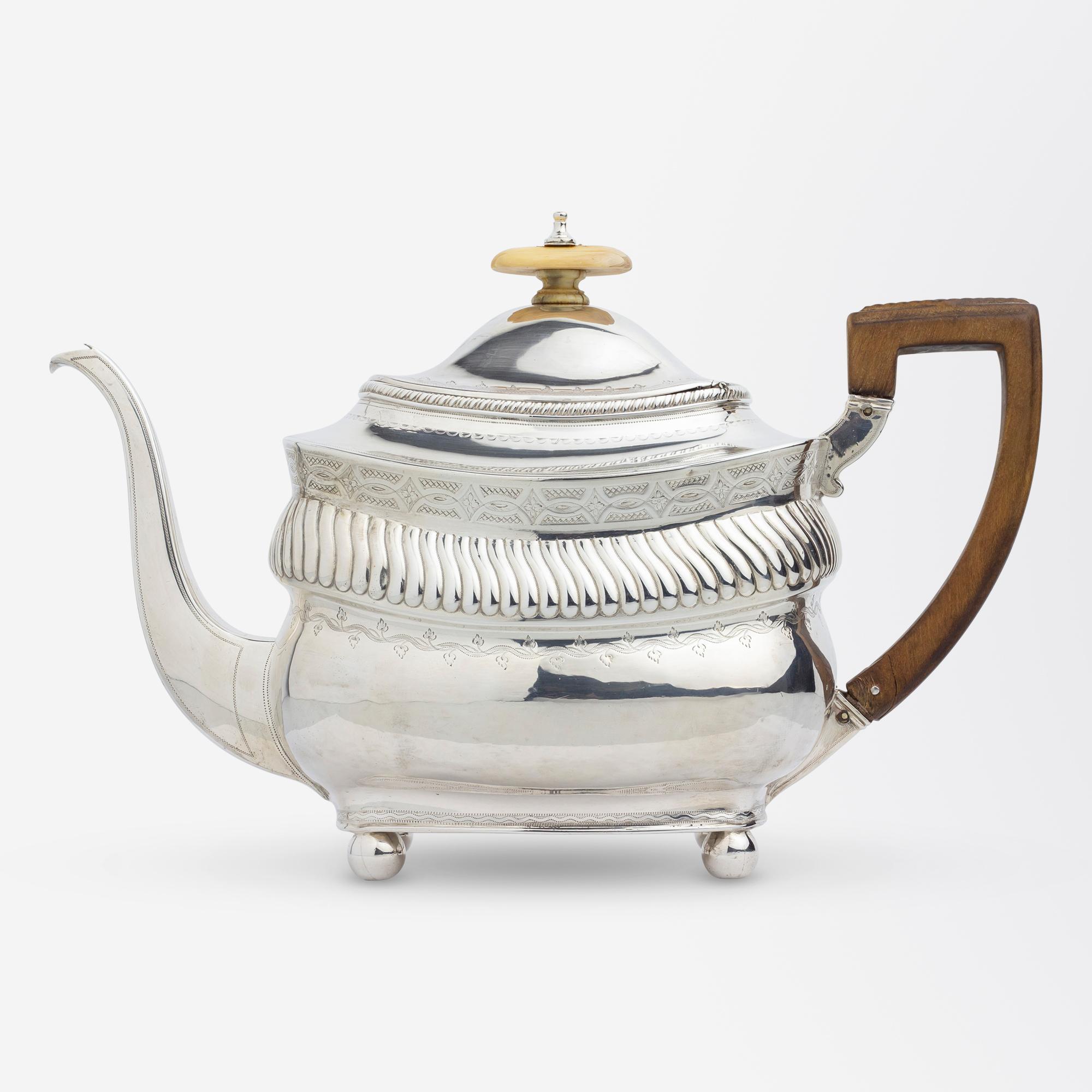 A sterling silver teapot with timber handle and bone finial by Peter & William Bateman of the famed silversmithing Bateman family. The teapot sits atop ball feet and features engraved vines, a ribbed scalloped band, and a patterned frieze. To one