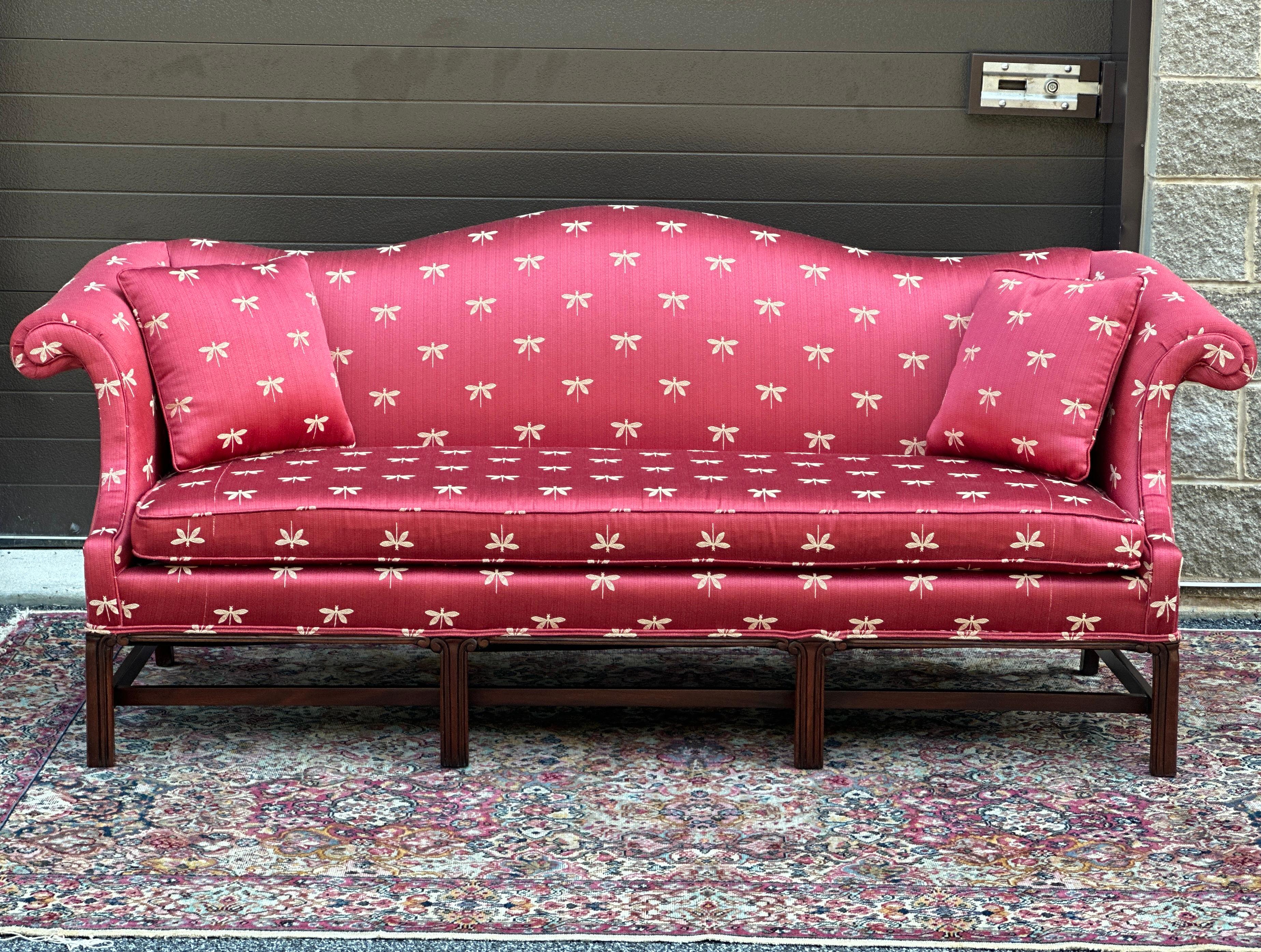 Classic high end camelback sofa by Hickory Chair Co. featuring a hand carved solid mahogany base and re-upholstered in dragonfly motif fabric. Two matched throw pillows included.