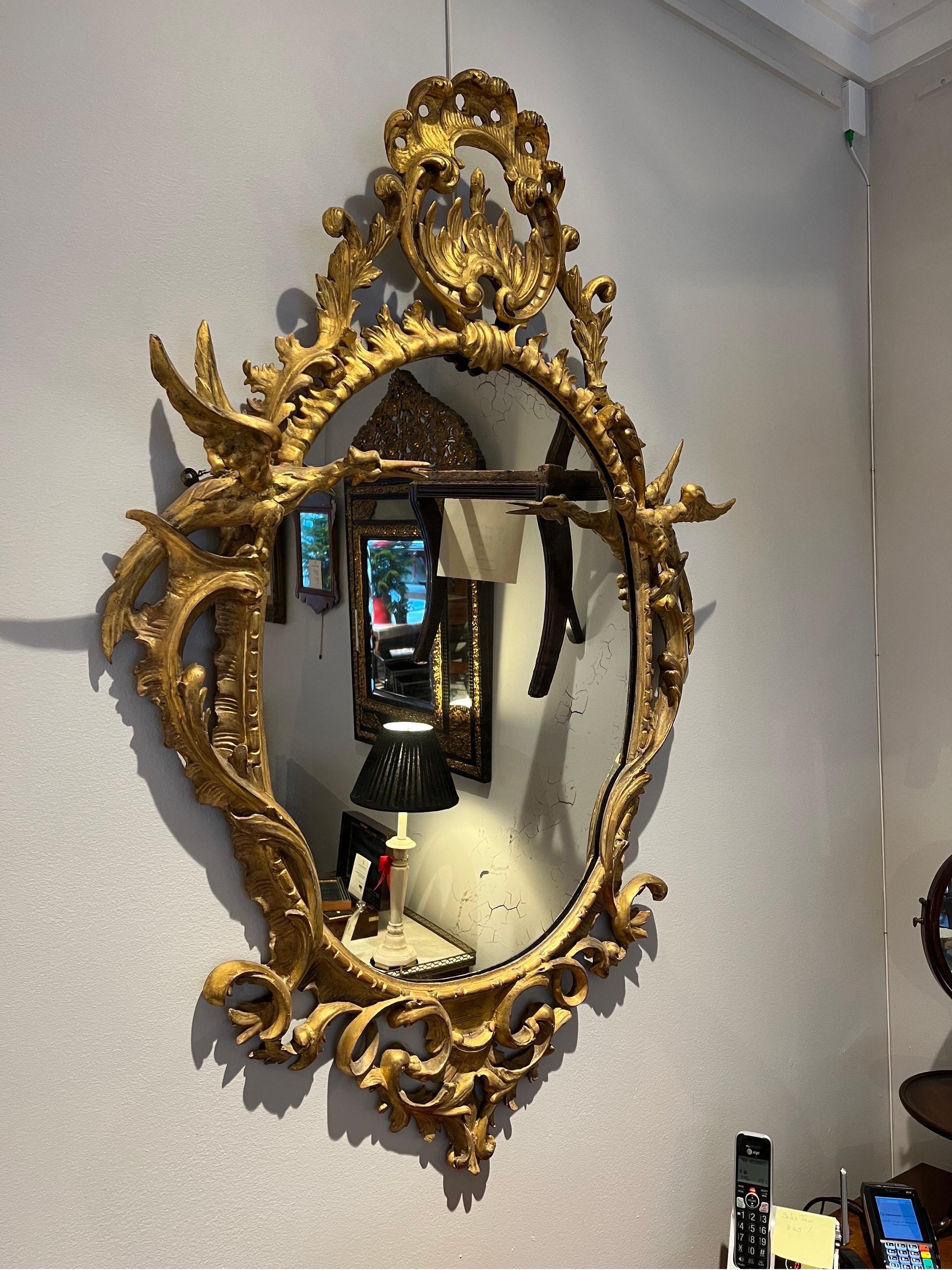 Spiegel aus vergoldetem Holz im Stil von George III. Mit einer ovalen Spiegelplatte, 
umgeben von einem blattgeschnitzten Goldholz-Ruhm. Der ovale Rahmen 
mit 2 geschnitzten Ho-Ho-Vögeln unterhalb der geschnitzten mit einer zentralen