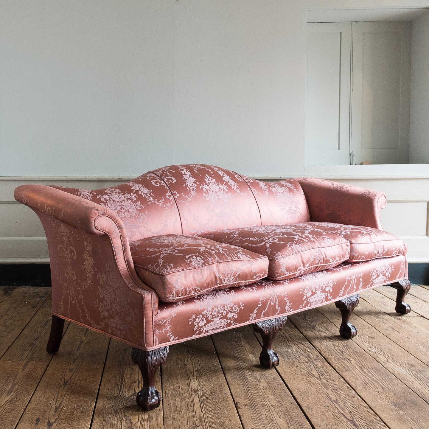 George III style humpback sofa, with scroll arms on four mahogany claw and ball feet, upholstered in rose pink silk damask with three feather-filled squab cushions.