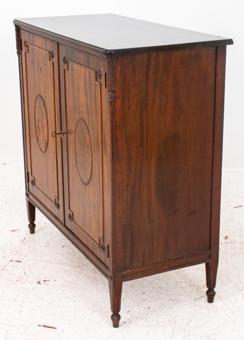 George III Style mahogany two door cabinet, rectangular molded top above two doors centering oval cartouches within canted rectangular molded framing, opening to reveal shelves, on short tapering square legs on casters. 

Dimensions: 43