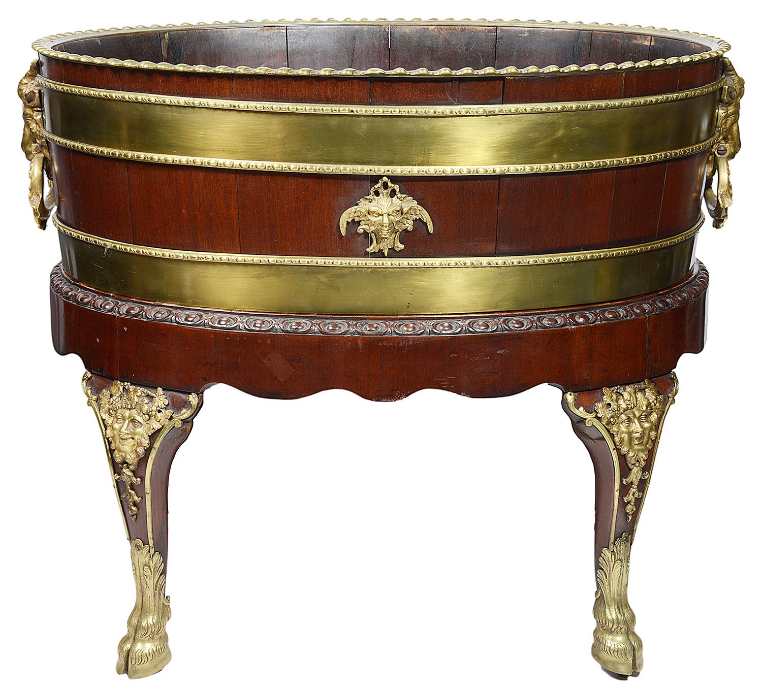 A George III style gilt-lacquered brass-mounted mahogany wine cooler
After Samuel Norman, circa 1765.
The oval body with gadrooned rim , bound by two bands with cabochon edges, each side mounted with a winged mask and the ends with goat masks
