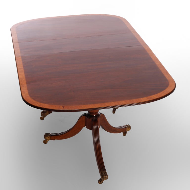 A Georgian style extension and tilt-top dining table offers mahogany construction with cross banded top over double pedestal base with Duncan Phyfe reeded legs terminating in cast brass paw feet, accepts single leaf, c1940

Measures - 30.25''h x