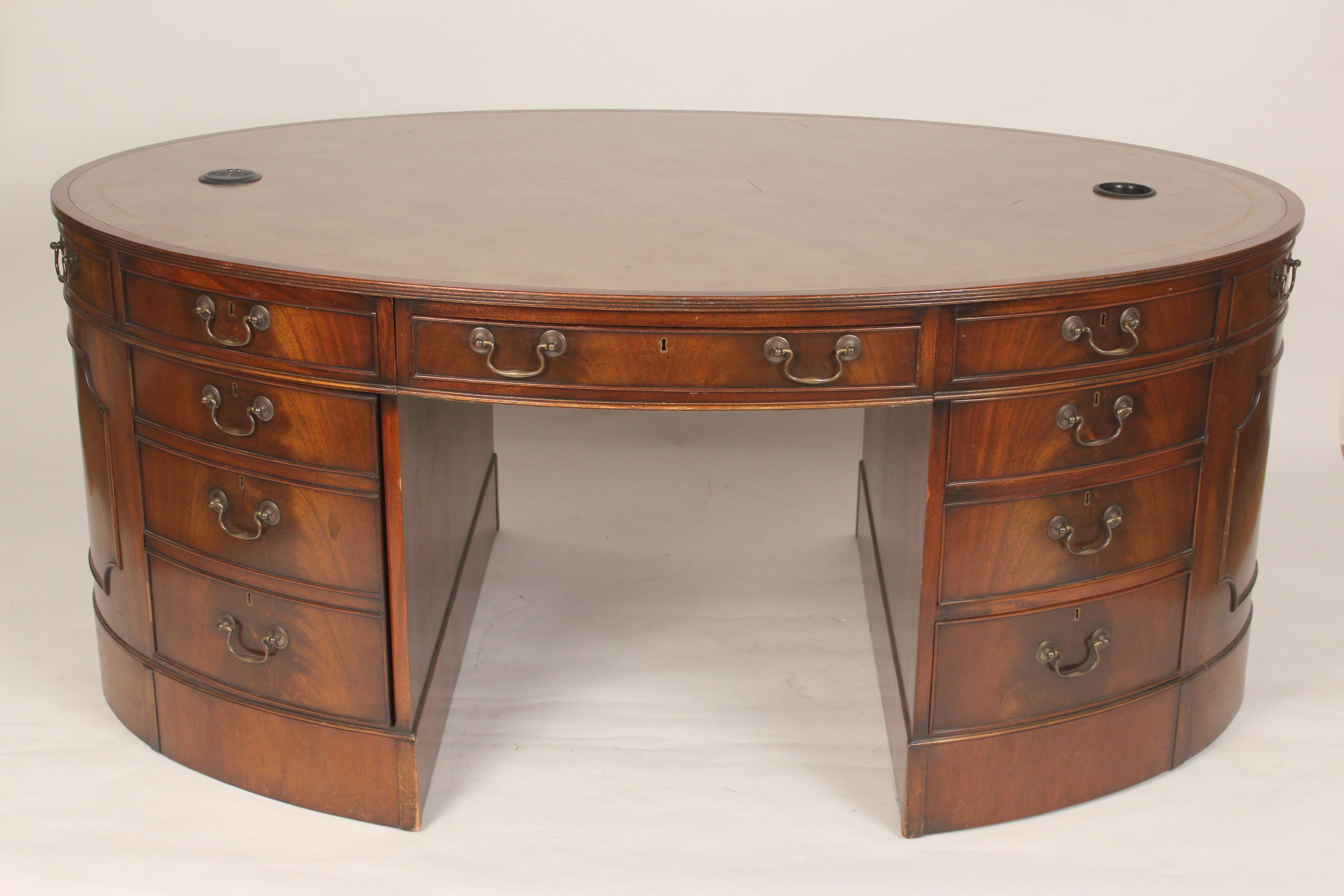 George III style oval mahogany partners desk with a tooled leather top, mid 20th century. Having nicely figured mahogany, hand dove tailed drawer construction and English lever locks. There are two circular areas on the top, one has an electrical