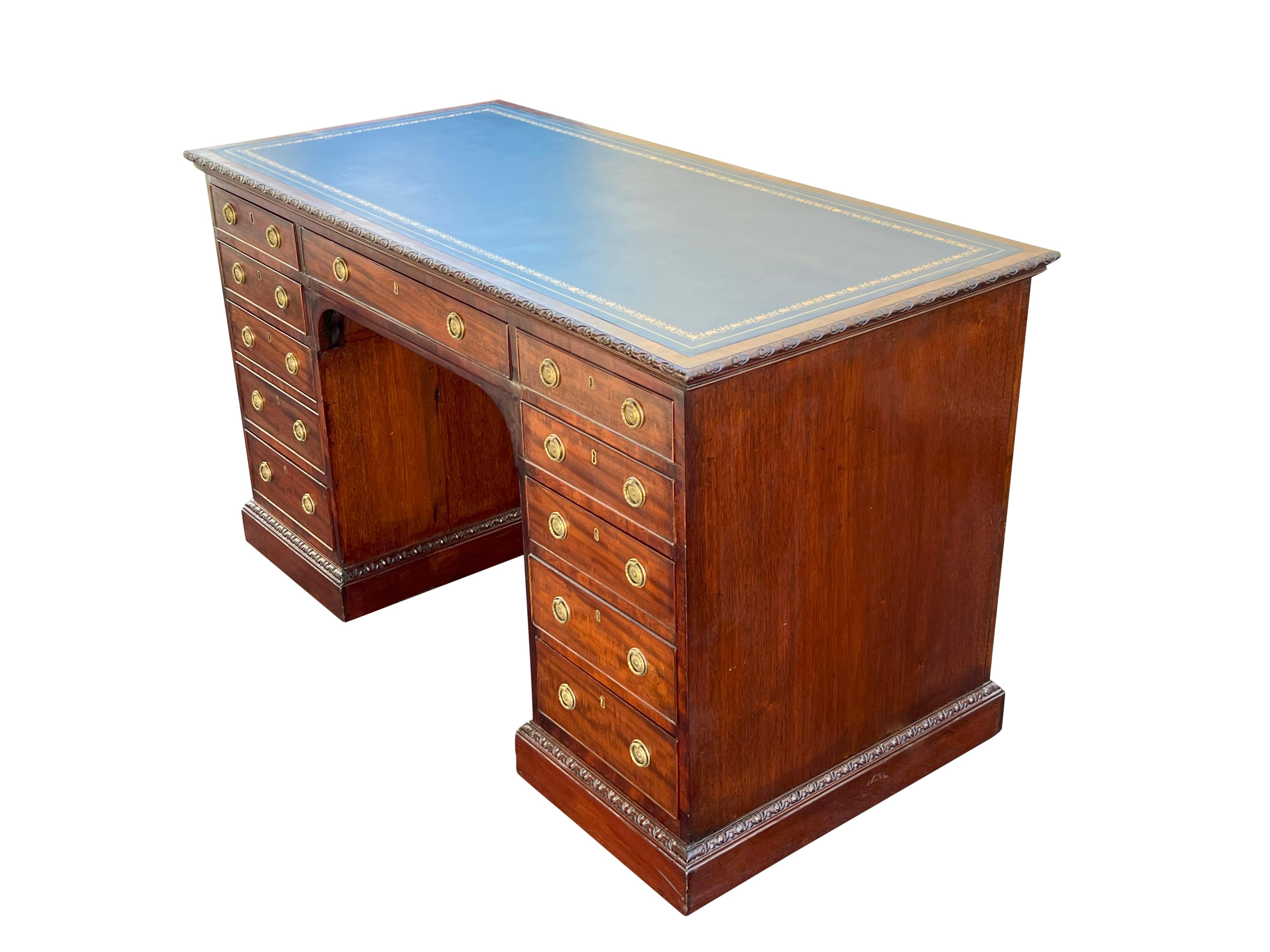 Rectangular top with new blue tooled leather inset and carved edge detail. Below a long drawer flanked by two small drawers over a kneehole with three drawers on one side and four on the other. Finished on back. From a Newport RI estate.