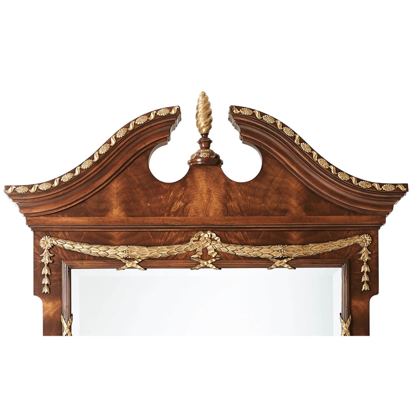 A carved mahogany, flame mahogany veneered and parcel-gilt wall mirror, the arched broken swan neck crest with a carved molding and centered by a spiral carved pinecone finial, the rectangular beveled edge mirror below framed by a bound reed slip