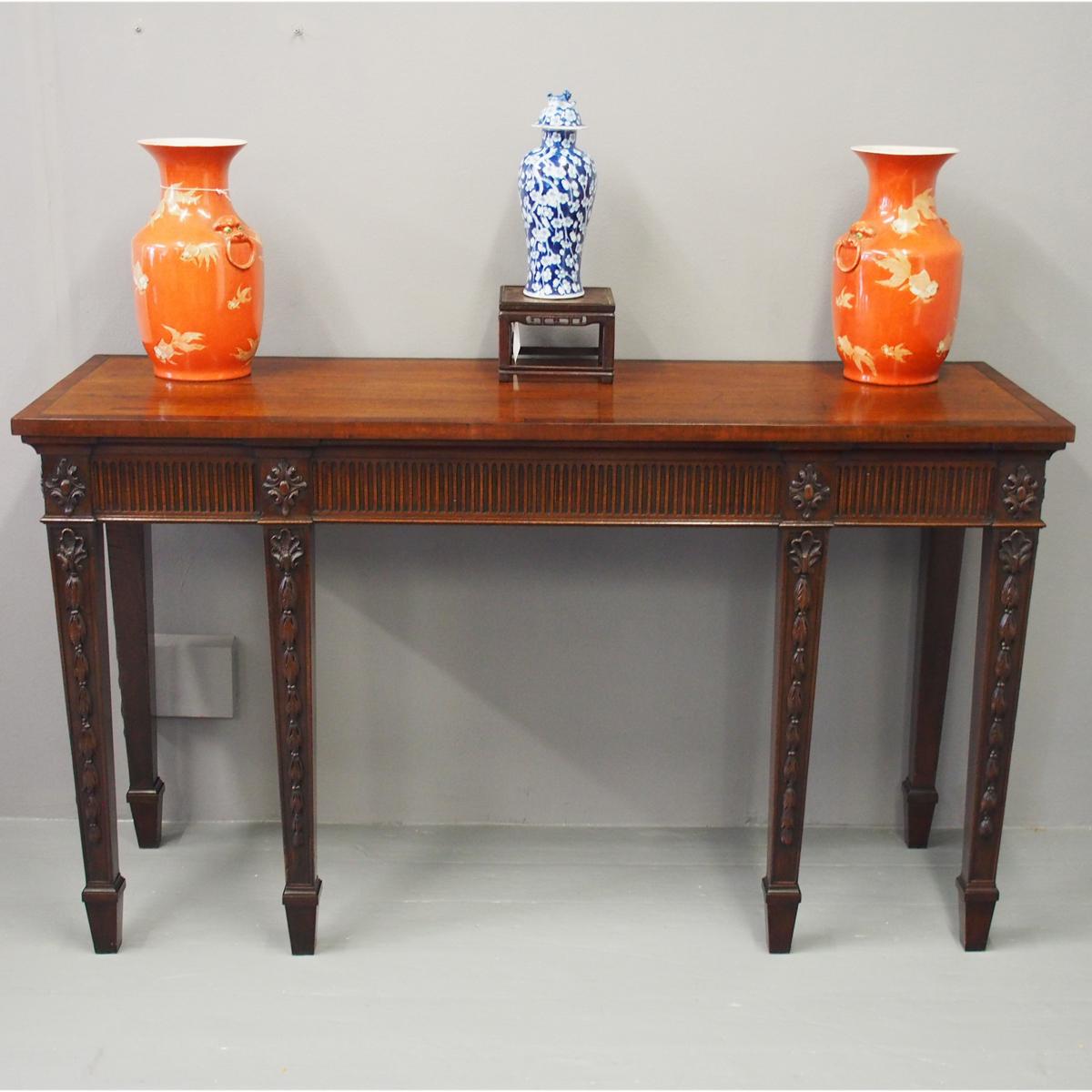 George III style mahogany serving table, circa 1880. With a later crossbanded top above a fluted frieze which is accented by foliate carved blocks above the legs. There are carved shells and husk trails to the front legs, and all legs are square and