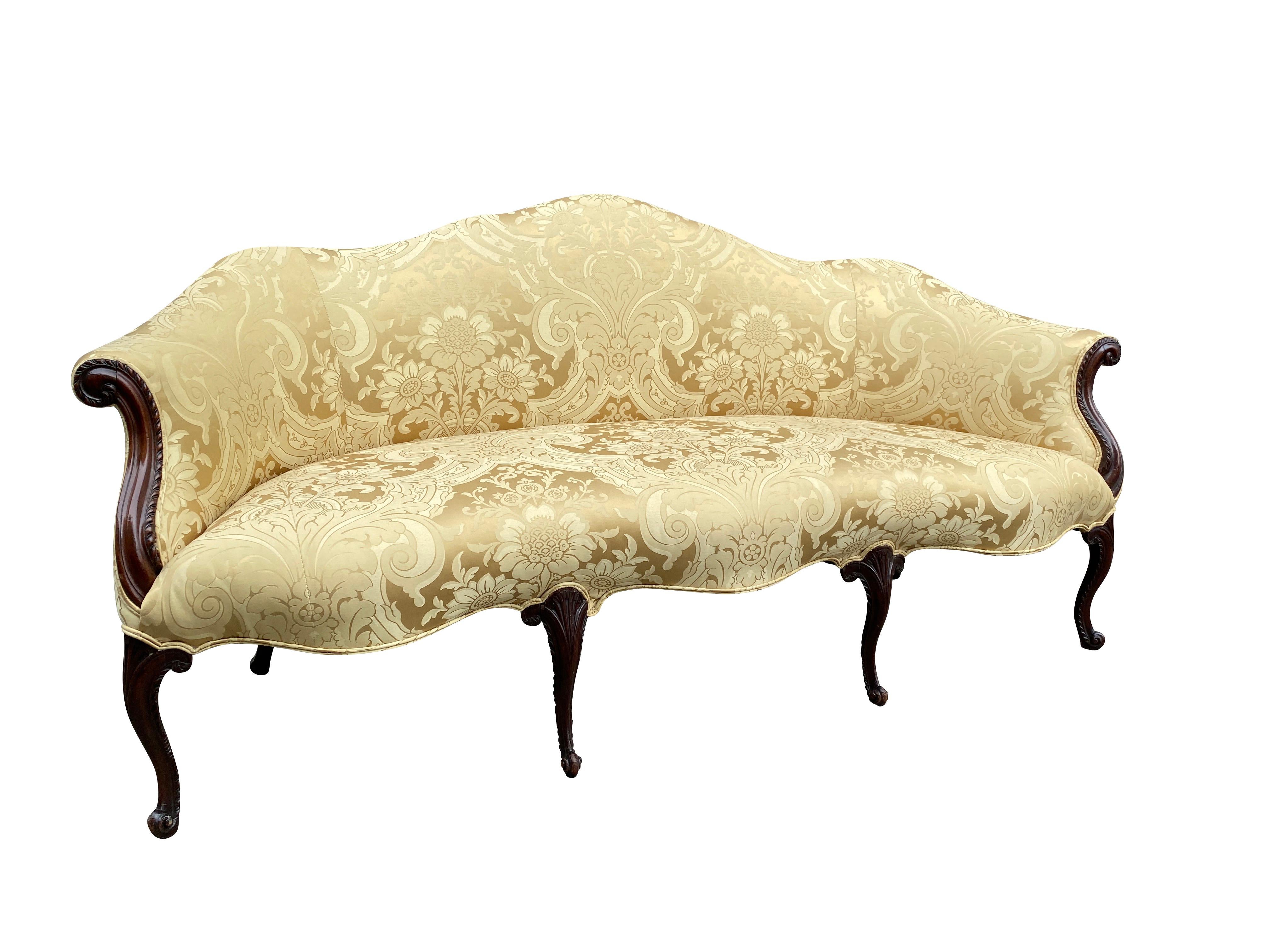 Serpentine upholstered back and seat done in yellow damask, scrolled arms and raised on carved cabriole legs in the French taste.