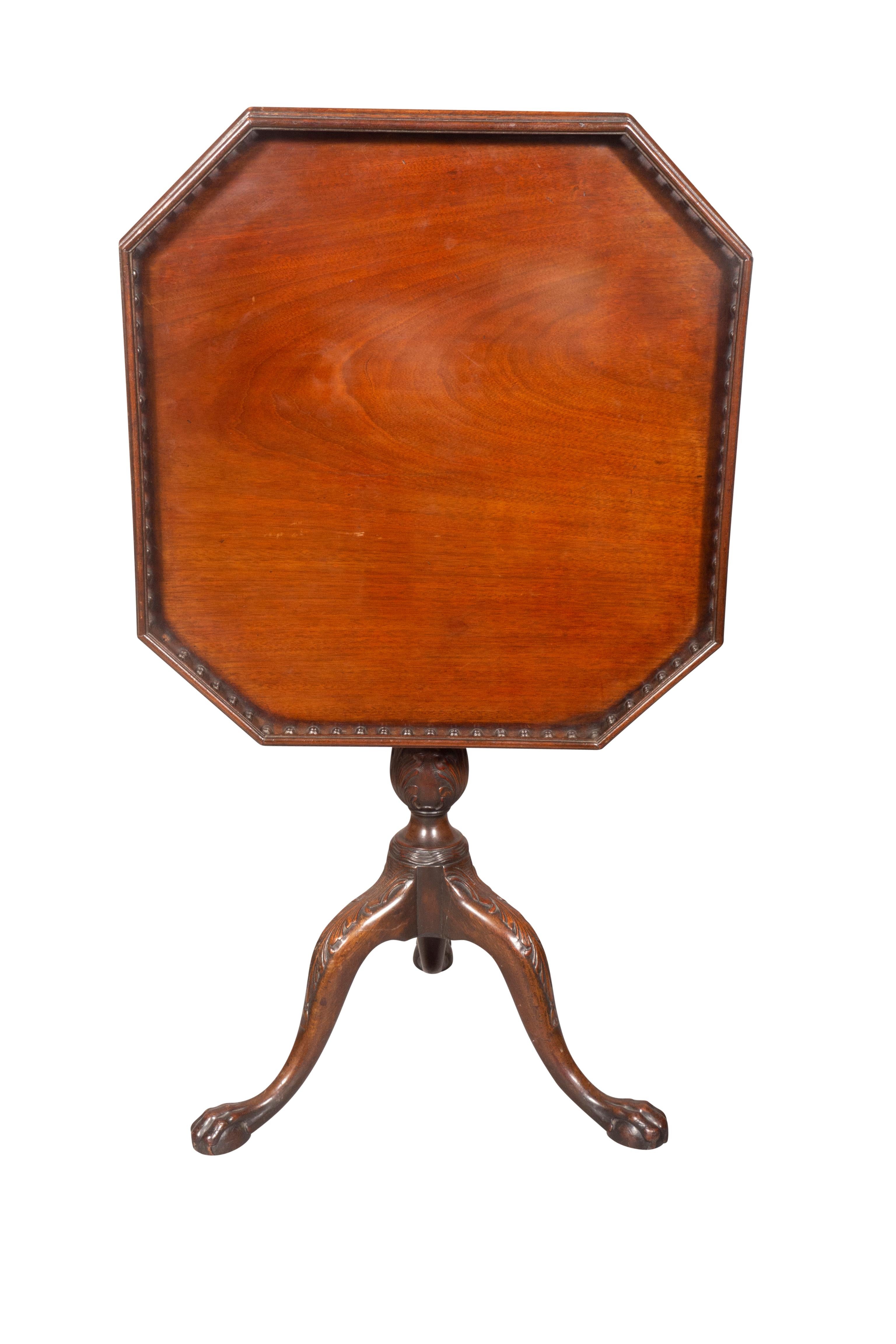 With octagonal hinged tilt top with spindle gallery on a carved support with gothic and leaf design carved details, three cabriole legs and paw feet.