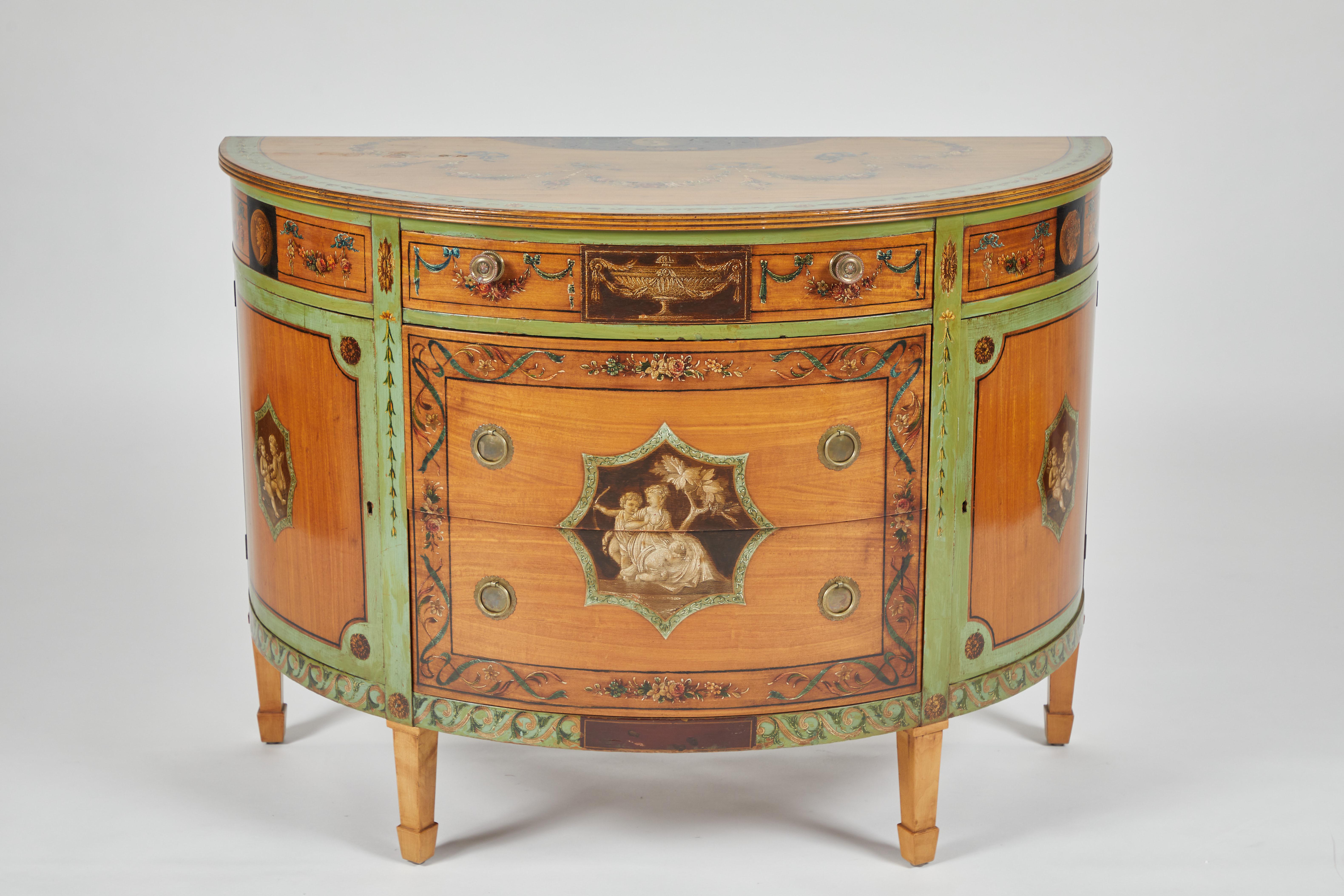 George III style parcel-painted satinwood cabinet. The demilune top centered by a bust in profile, the front with a central figure with a cupid at her side and a putti at her knees surmounted by an urn draped with swags of foliage, the conforming