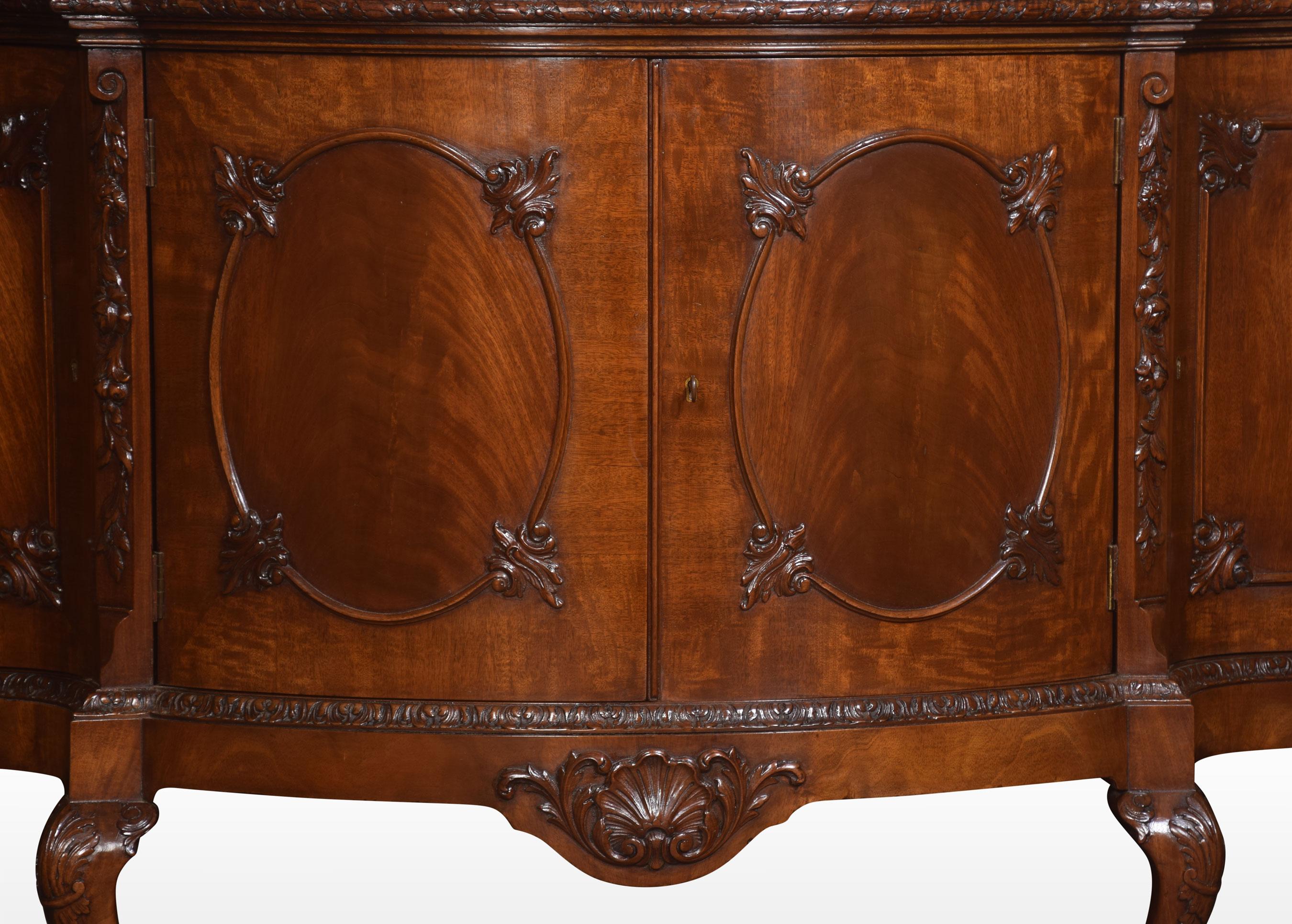 Mahogany sideboard, the large serpentine top with a carved rim. Above two oval moulded mahogany paneled doors opening to reveal large fixed shelf. Flanked by two similar cupboards. All raised up on four cabriolet legs terminating in claw and ball