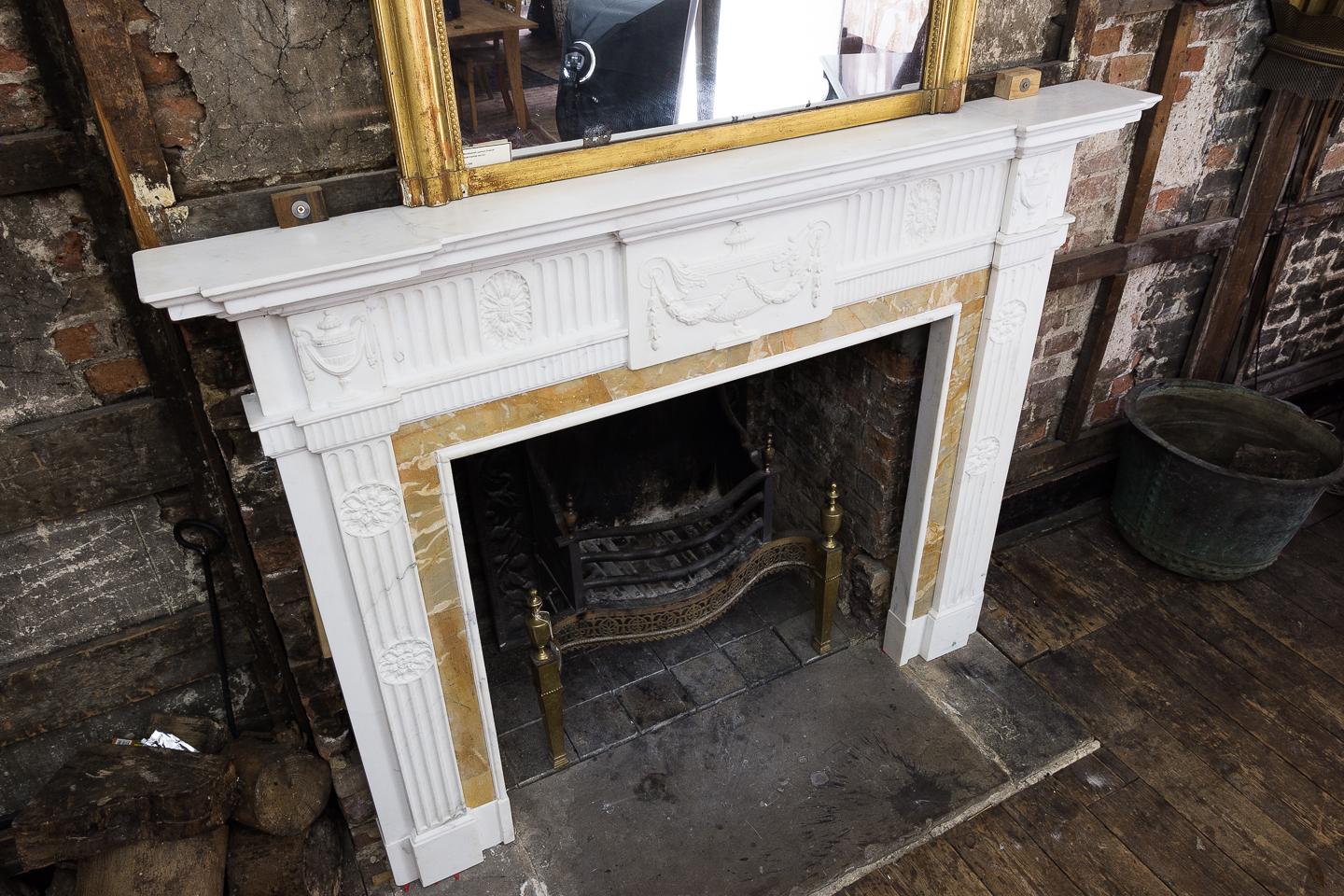 A George III style statuary and sienna marble neoclassical chimneypiece, possibly Irish, early 20th century, the inverse breakfront moulded shelf above tablet with classical tazza carved in relief flanked by fluted frieze centred by oval paterae,