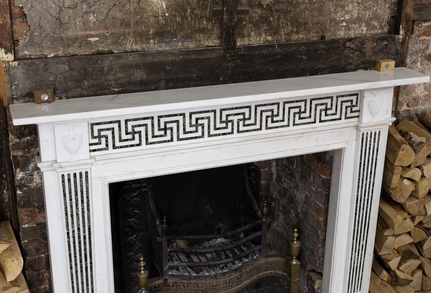 George III style white marble and inlaid chimneypiece, the plain rectangular shelf above Greek-key pattern frieze of Verde marble, flanked by classical ewer endblocks, the tapered pilaster jambs with further Verde marble inlay, raised on square