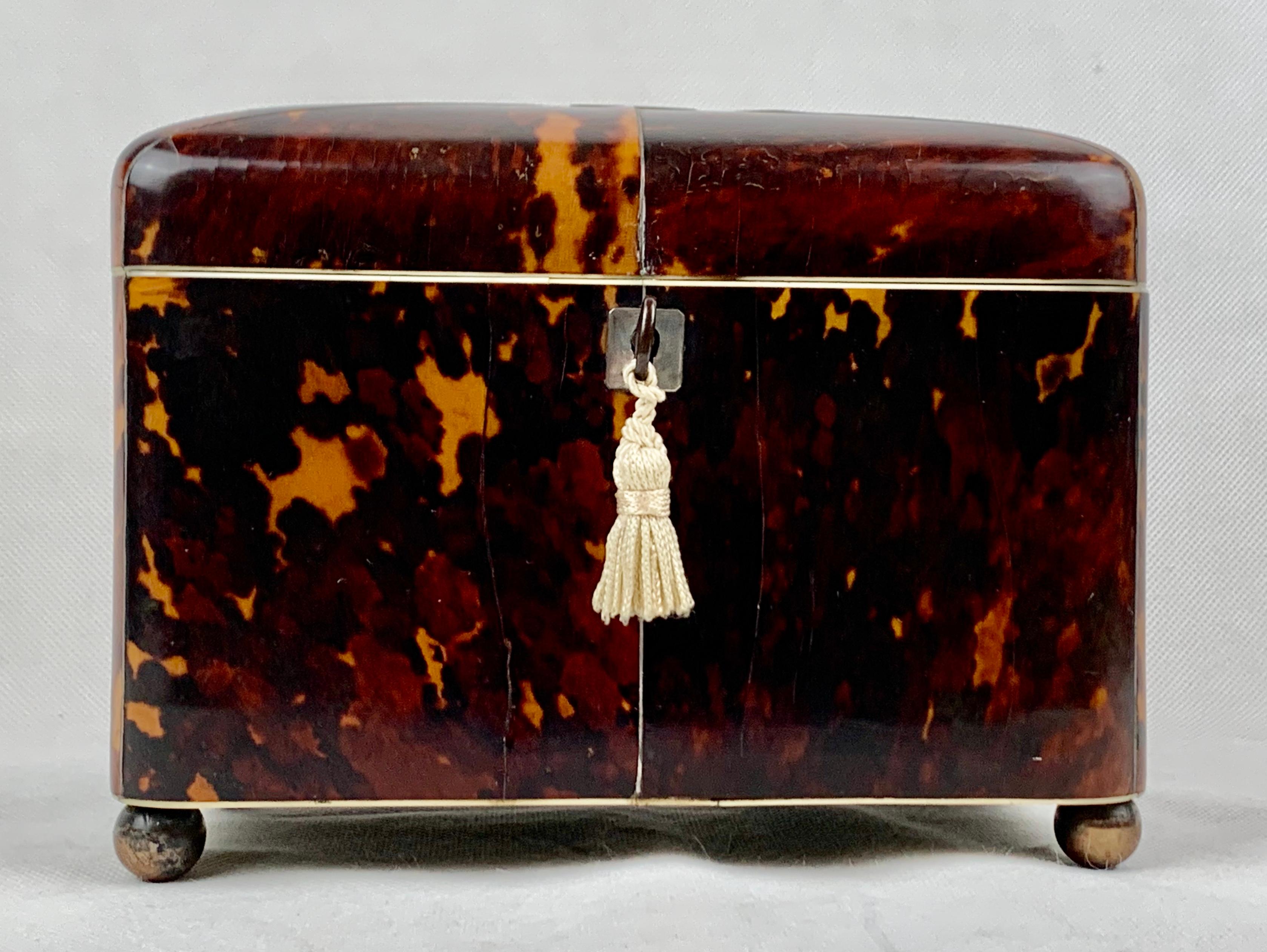 Geoerge III tortoiseshell tea caddy.  The dome top is decorated with a silver monogram plate and silver stringing from each corner to the center plate.  The front has a silver escutcheon plate and key.  The totally original interior has red velvet