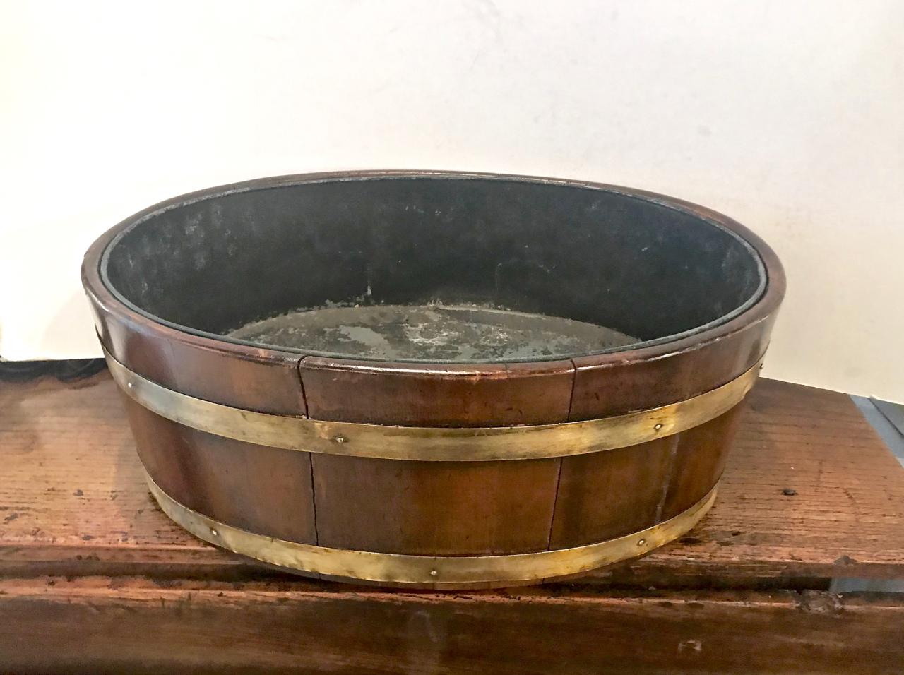 This is a very decorative late George III brass bound mahogany wine cooler. The wine cooler is in very good overall condition with minor old professional restorations and an old replaced liner.
The cooler would make a stunning planter or jardinière