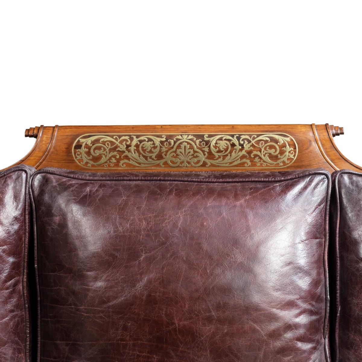 A George IV brass inlaid rosewood country house three-seat sofa attributed to Gillows, the serpentine back with a central panel and gadrooned terminals at either end, the carved scrolling arms continuous with the panelled seat rail, decorated with