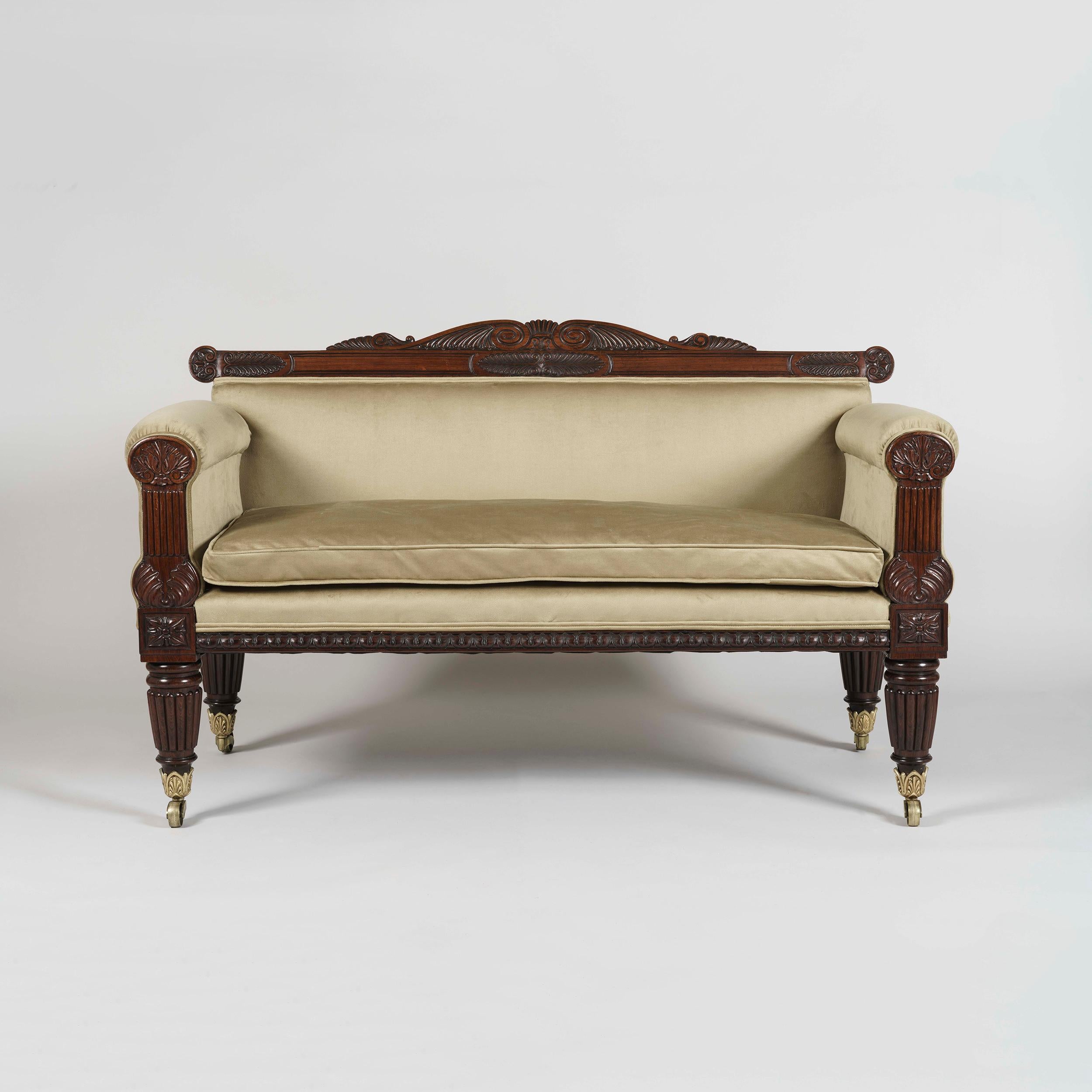 A superb George IV period sofa
In the Grecian Manner

Carved from richly colored rosewood, the rectilinear sofa designed in the Grecian manner, supported on four reeded and tapering legs with brass casters; the shaped end supports having tablets,