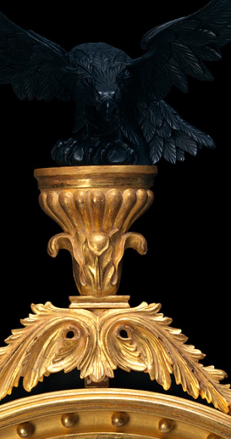 An imposing large Regency convex mirror with carved wood cornucopia style electrified candle arms, the ball decorated moulded frame surrounded by vine leaf and grape decoration and surmounted by an ebonised eagle upon a raised platform. Bespoke
