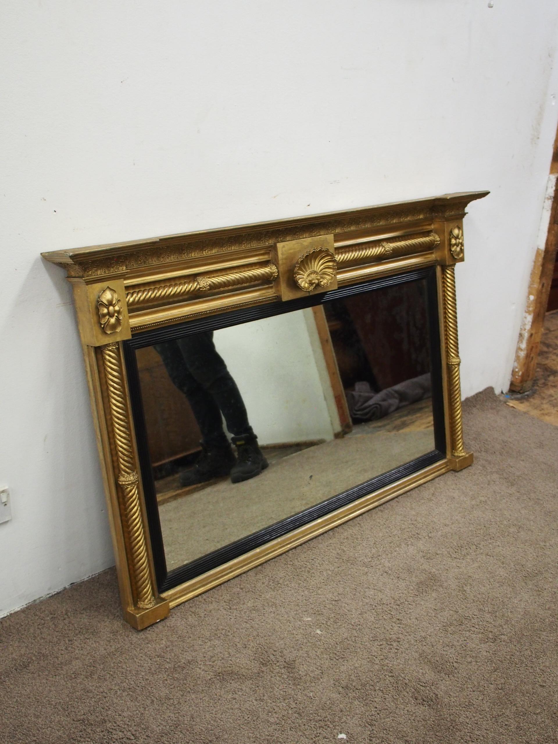 George IV gilded and ebonized overmantel mirror, circa 1820. It has a breakfront section, with a foliate decorated cornice and a central carved and gilded shell. To either side are barley sugar twists, finishing on foliate bezels and the mirror
