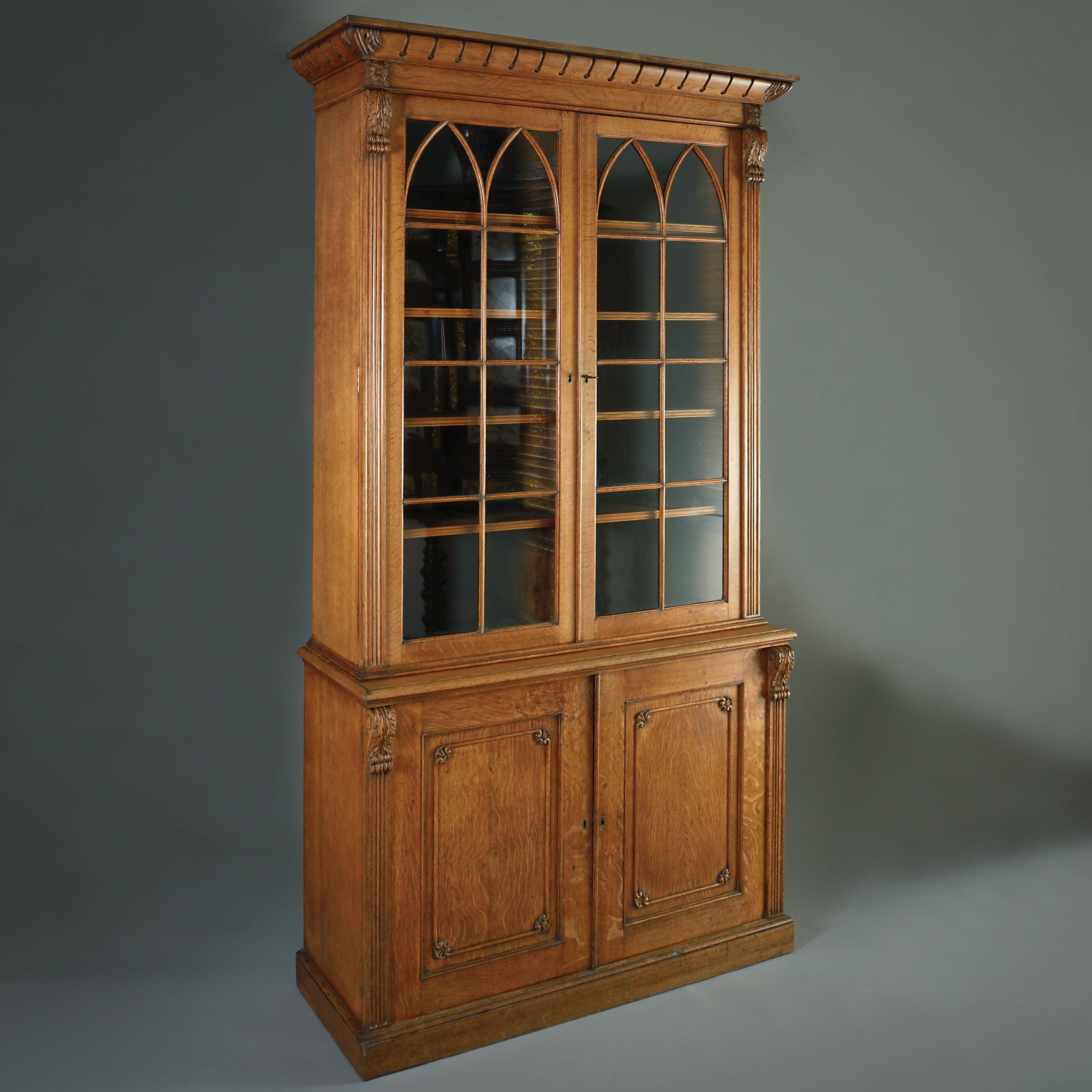 A GEORGE IV GOTHIC GOLDEN OAK BOOKCASE, CIRCA 1830.

With two glazed doors enclosing adjustable shelves above two panelled doors enclosing further adjustable shelves.