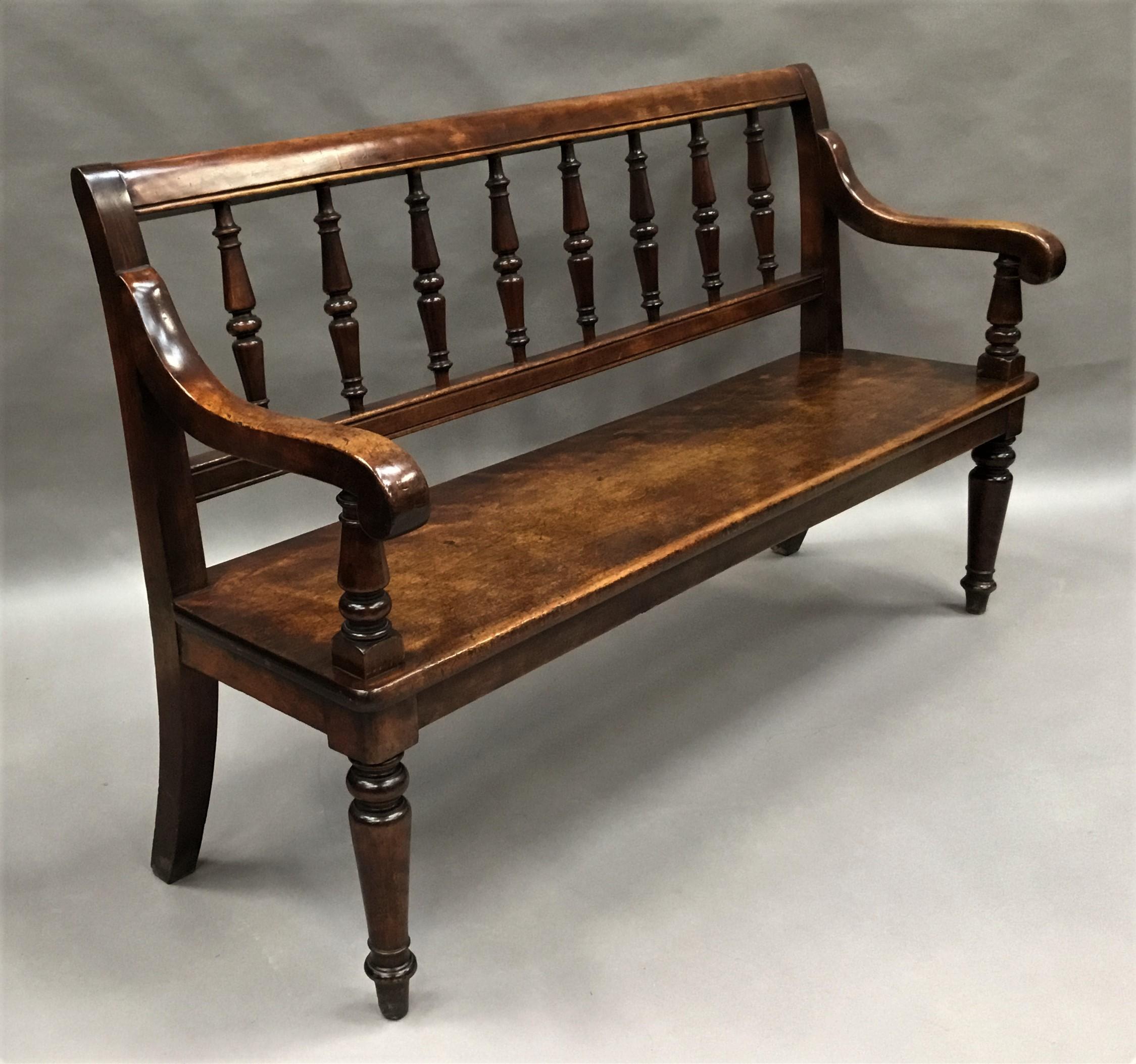 George IV birch hall seat or hall bench of bold proportions, the well figured molded top rail above 8 turned balluster spindles. The scrolled arms on tapering supports, raised on the solid rectangular seat with sabre legs to the reverse and turned