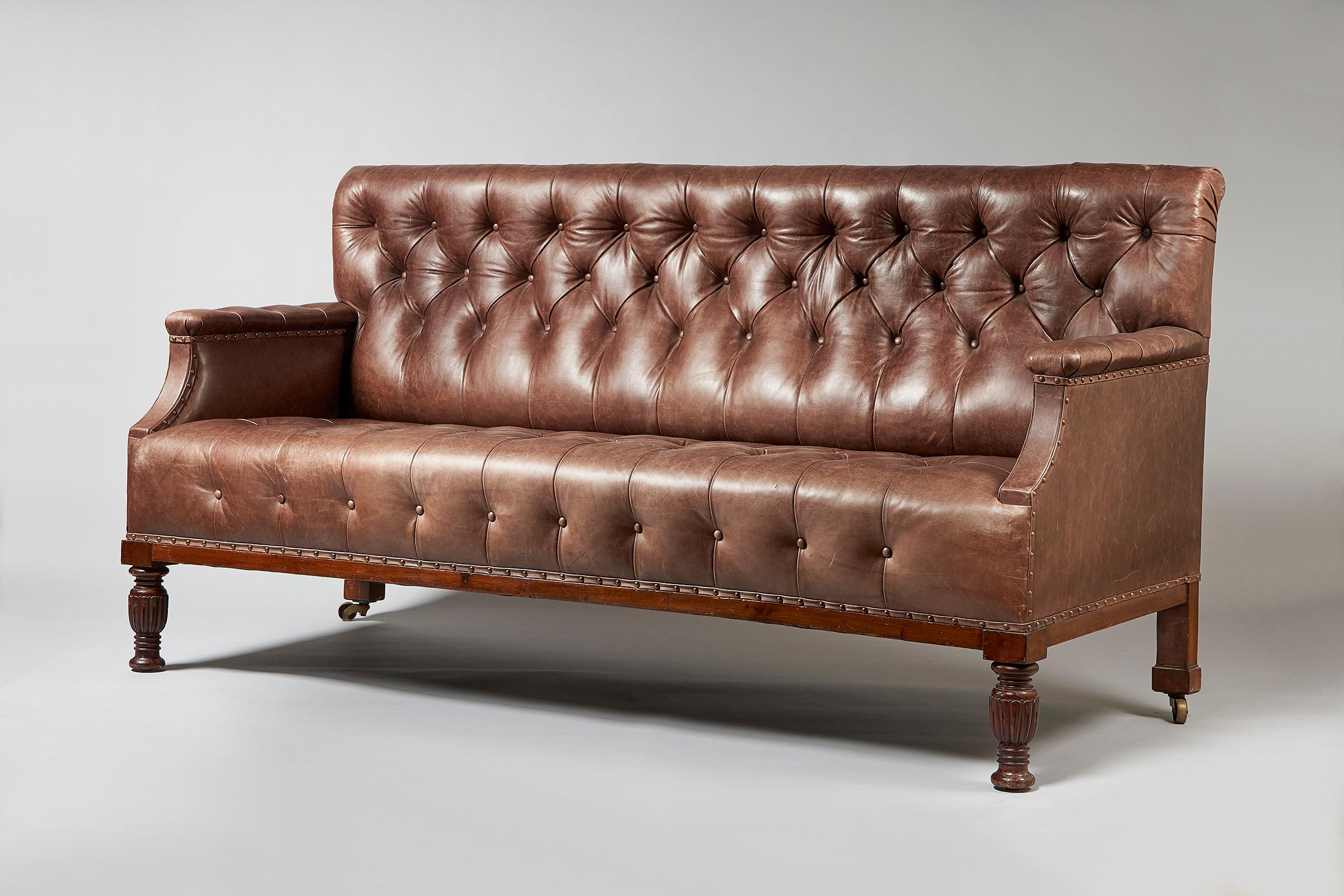 A George IV leather club sofa, early 19th century with straight back and arms, turned wood legs, upholstered in dark brown leather, button and stud detail.