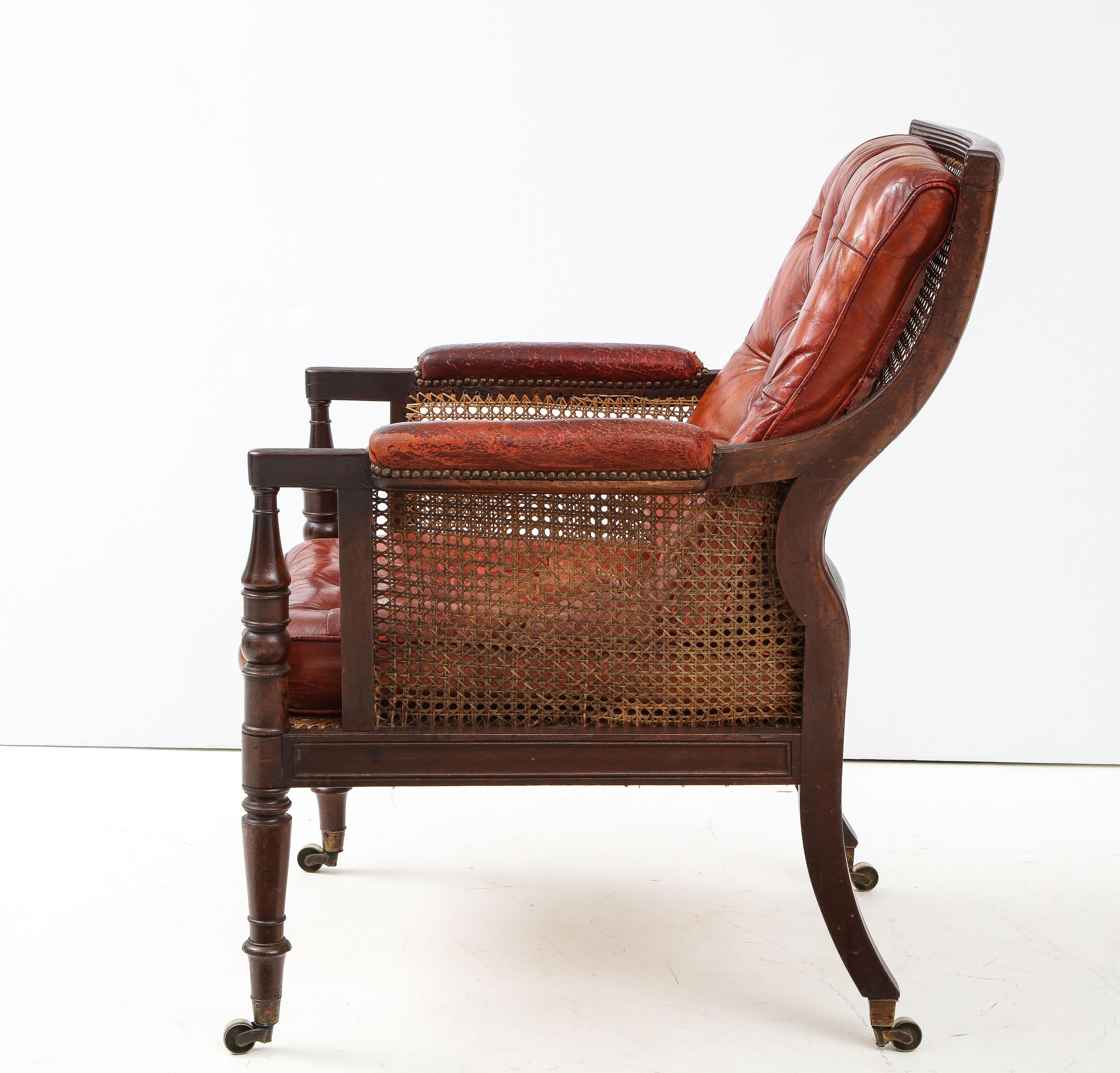 Fine George IV bergere the square back with ribbed rails and caning behind buttoned leather cushion, the armpads and seat similarly upholstered, the sides and seat also caned and standing on turned legs with original casters, the whole with good