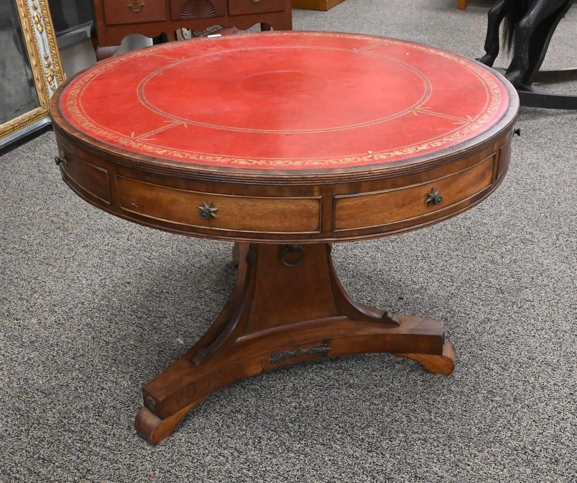 A George IV period center drum table in mahogany, circa 1840, with inset tooled leather top, with conforming drawers in the apron, on a pedestal base with tripod legs and scroll feet. 