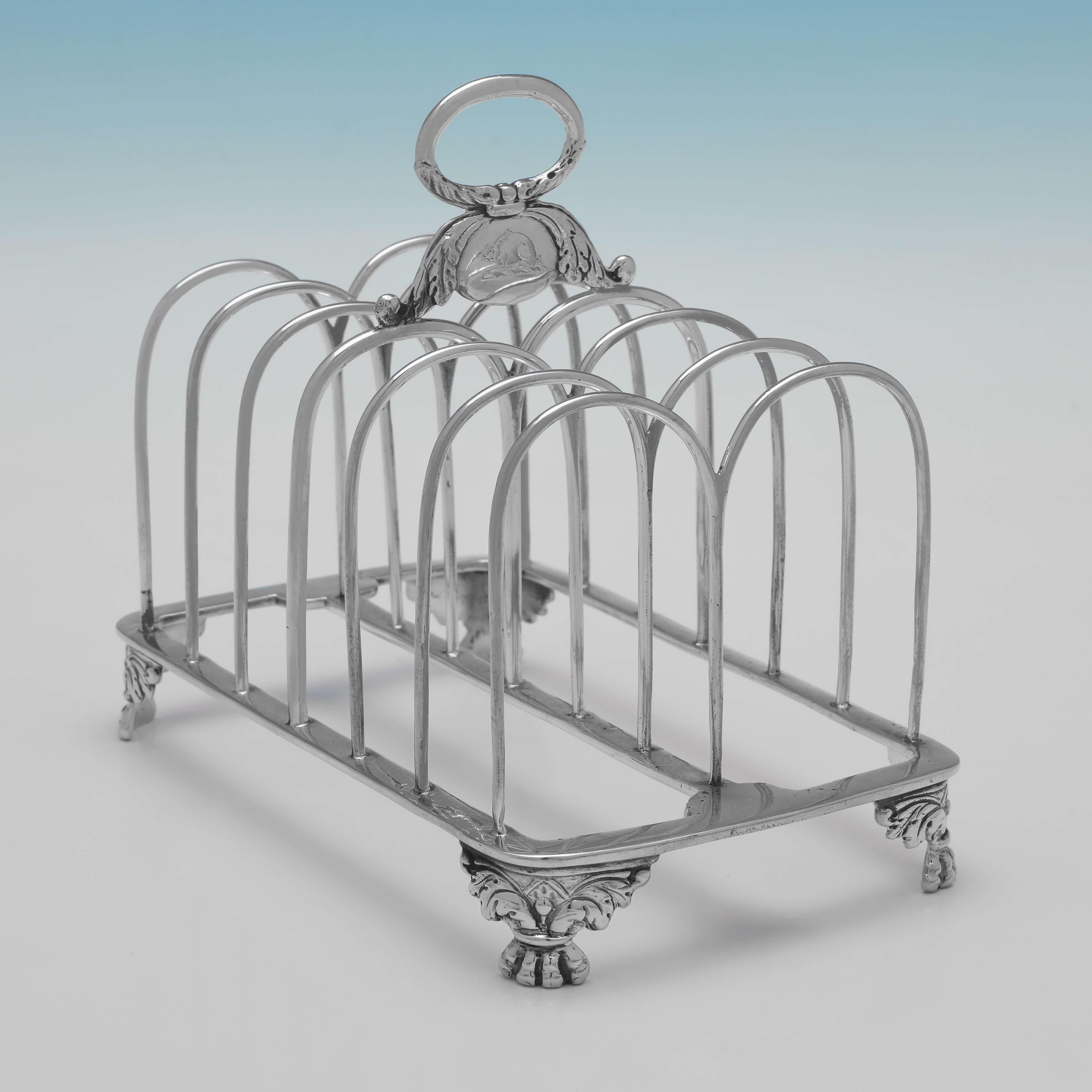 Hallmarked in London in 1823 by Samuel Whitford II, this stunning and rare pair of George IV period, Antique sterling silver toast racks, feature late Regency influenced decoration to the feet and handles, engraved crests of a hare to each handle,