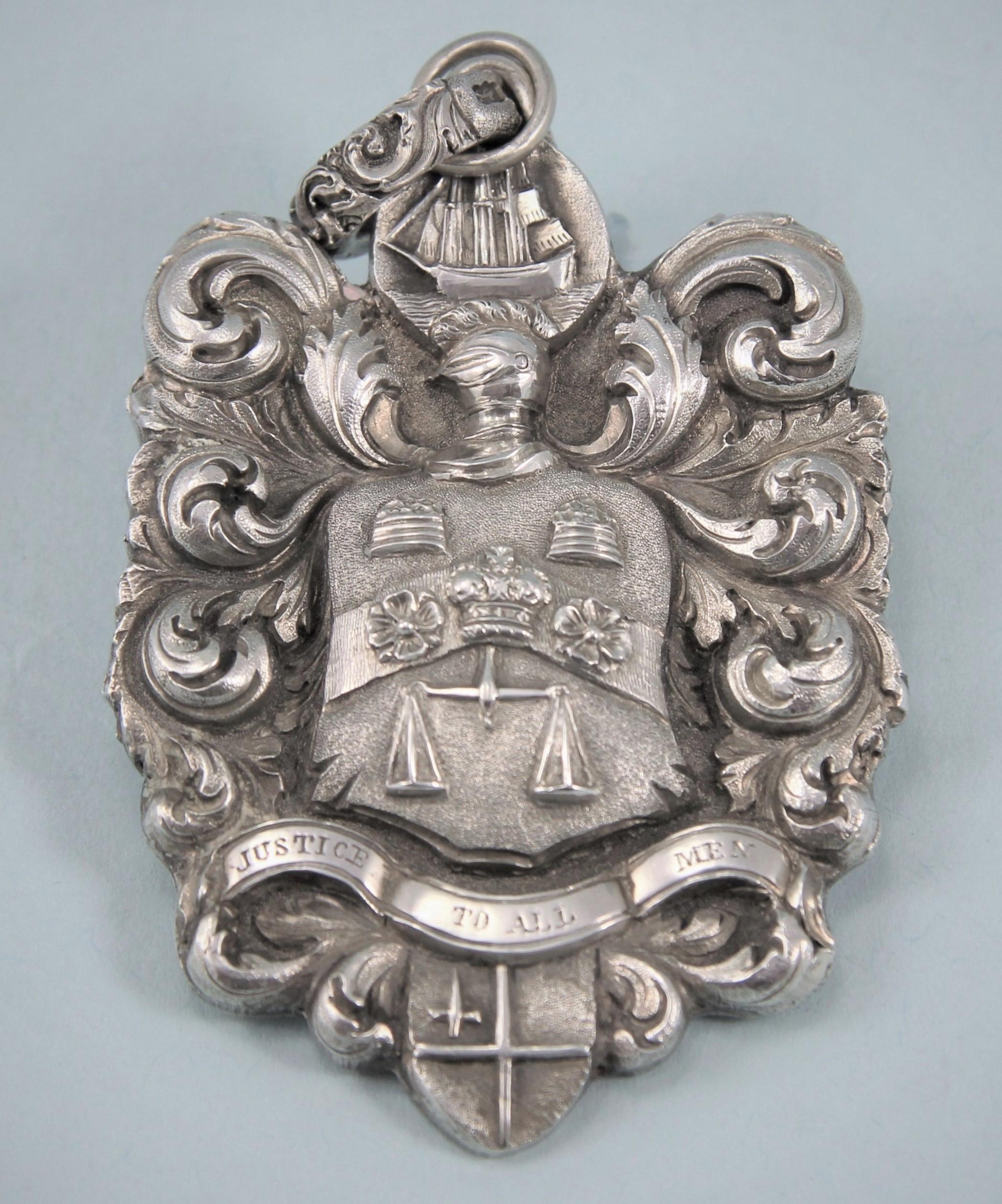 Interesting George IV silver sea-coal meter badge. Unmarked.
Maker's mark AD stamped on the ring attachment. England, circa 1824. 

The badge is of shaped form with foliate scroll decoration and an armorial with motto beneath in the centre. The