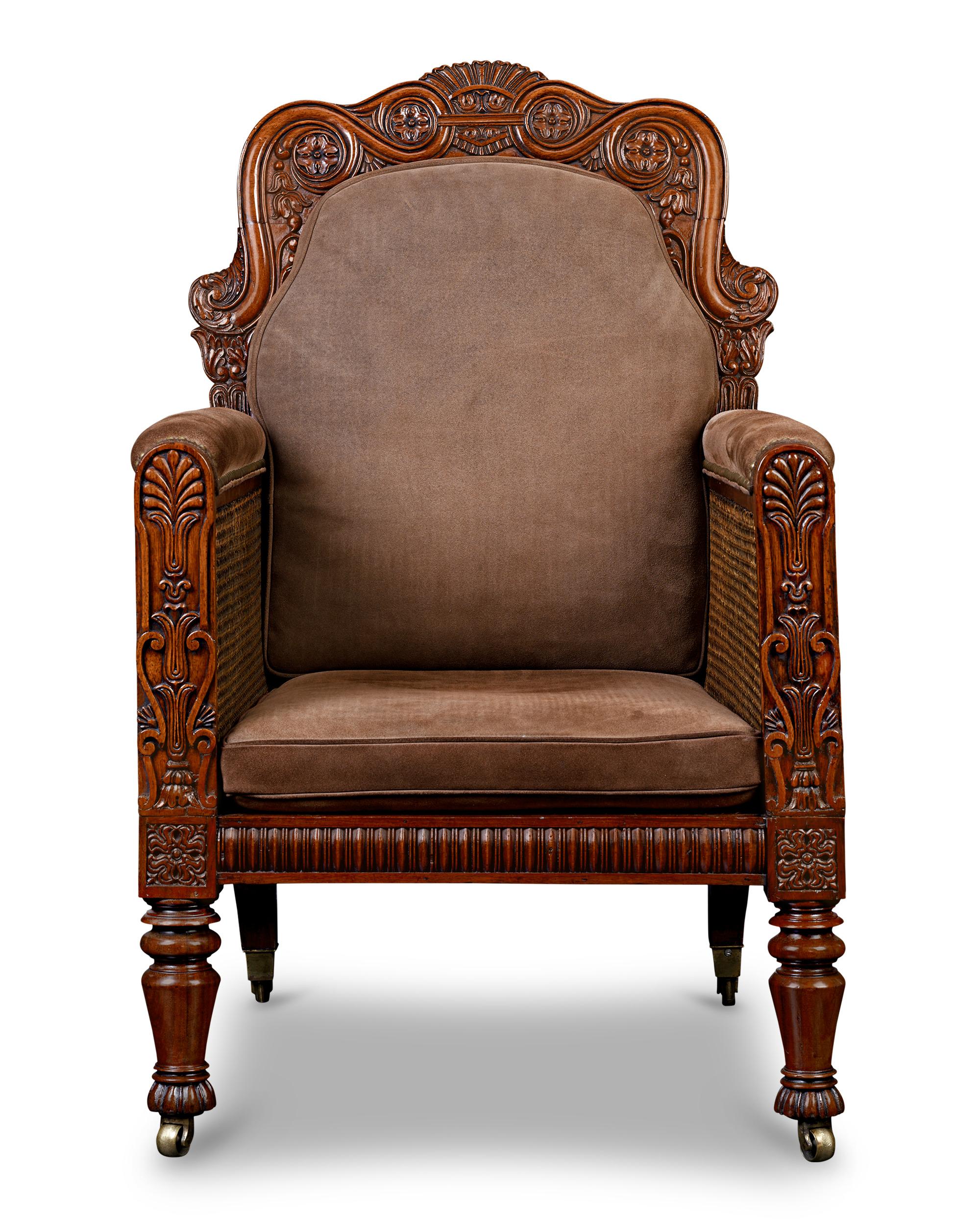 This stately George IV bergère armchair with caning details exudes elegance and sophistication. The armchair is crafted from walnut and features carved details and decorative elements, reflecting the neoclassical and Regency influences of the time.