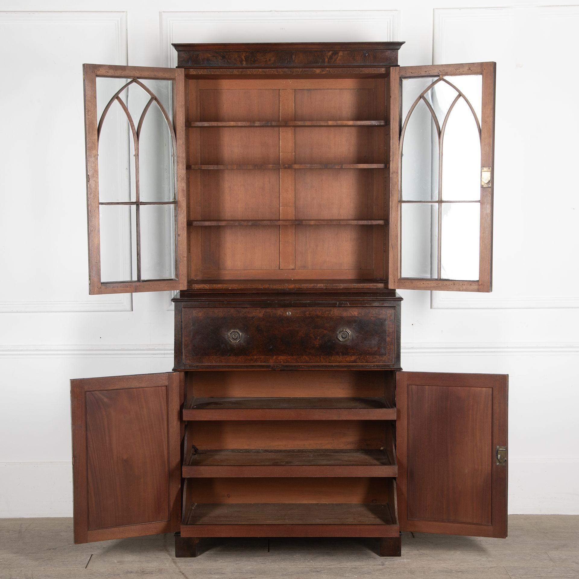 A George IV yew-wood veneered and crossbanded secretaire bookcase.
The upper part with a moulded cornice, fitted with adjustable shelves enclosed by a pair of Gothic pointed arch glazed panel doors.
The lower part having a hinged fall enclosing a