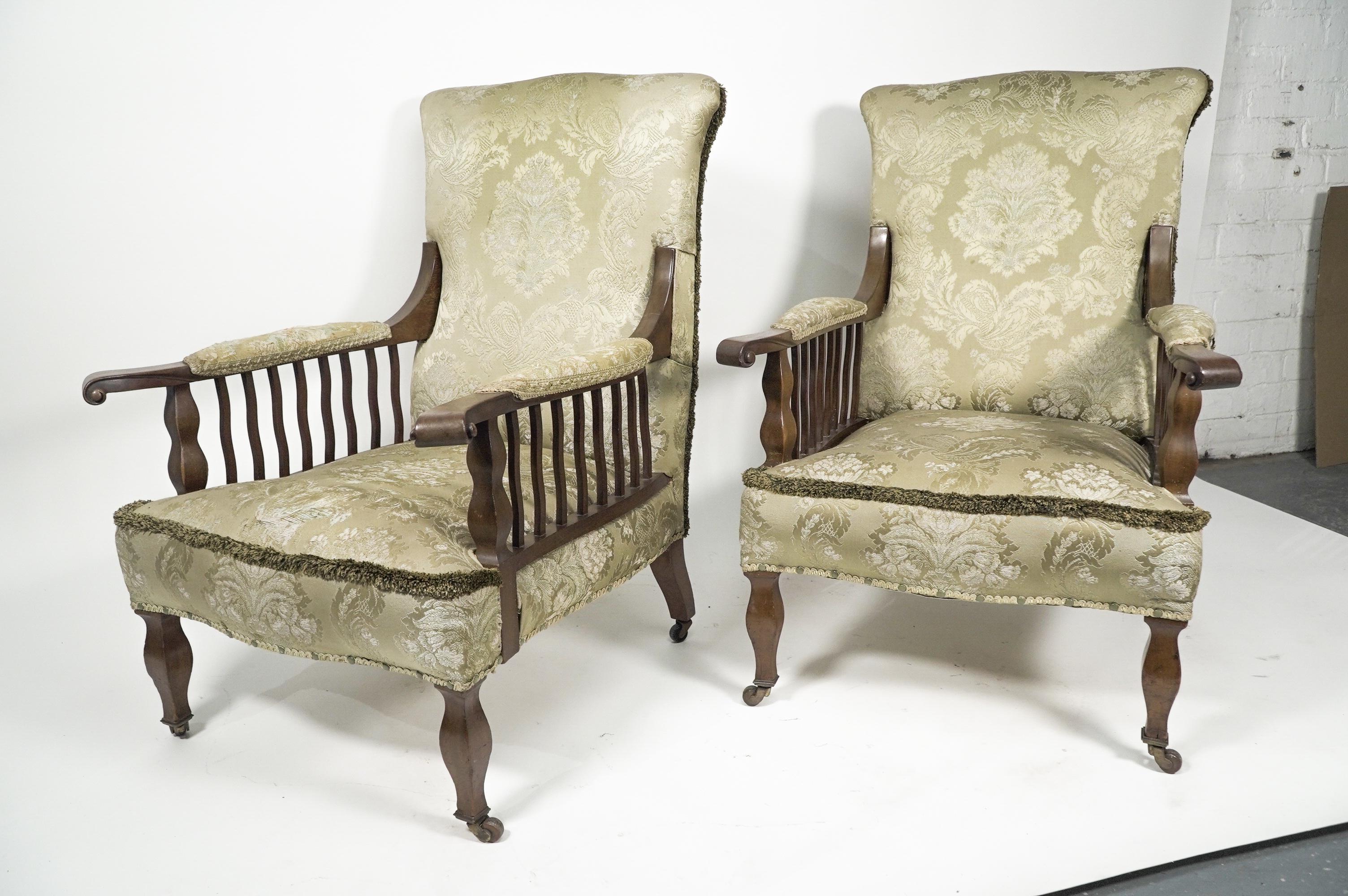Morris and Co, a pair of mahogany ‘Saville’ armchairs designed by George Washington Jack, with carved details to the arms and wavy spindles below and shaped support to the front matching the shaped front legs on brass and ceramic casters.
