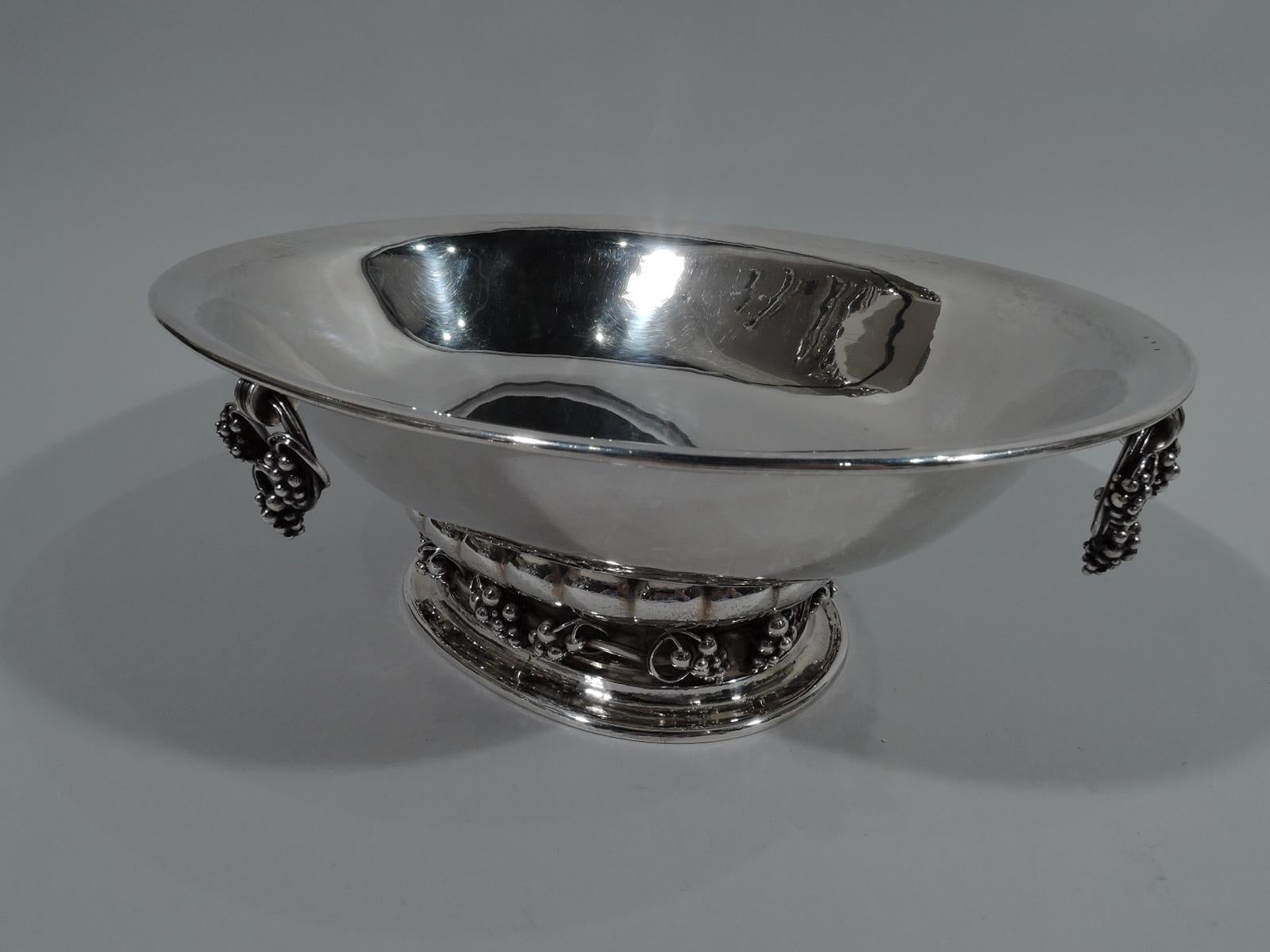 Modern sterling silver centerpiece bowl with classic grape motif. Made by Georg Jensen in Copenhagen. Oval bowl on lobed support with applied fruiting grapevine on flat oval foot. Rings entwined with bunches loose-mounted to each side. Fine