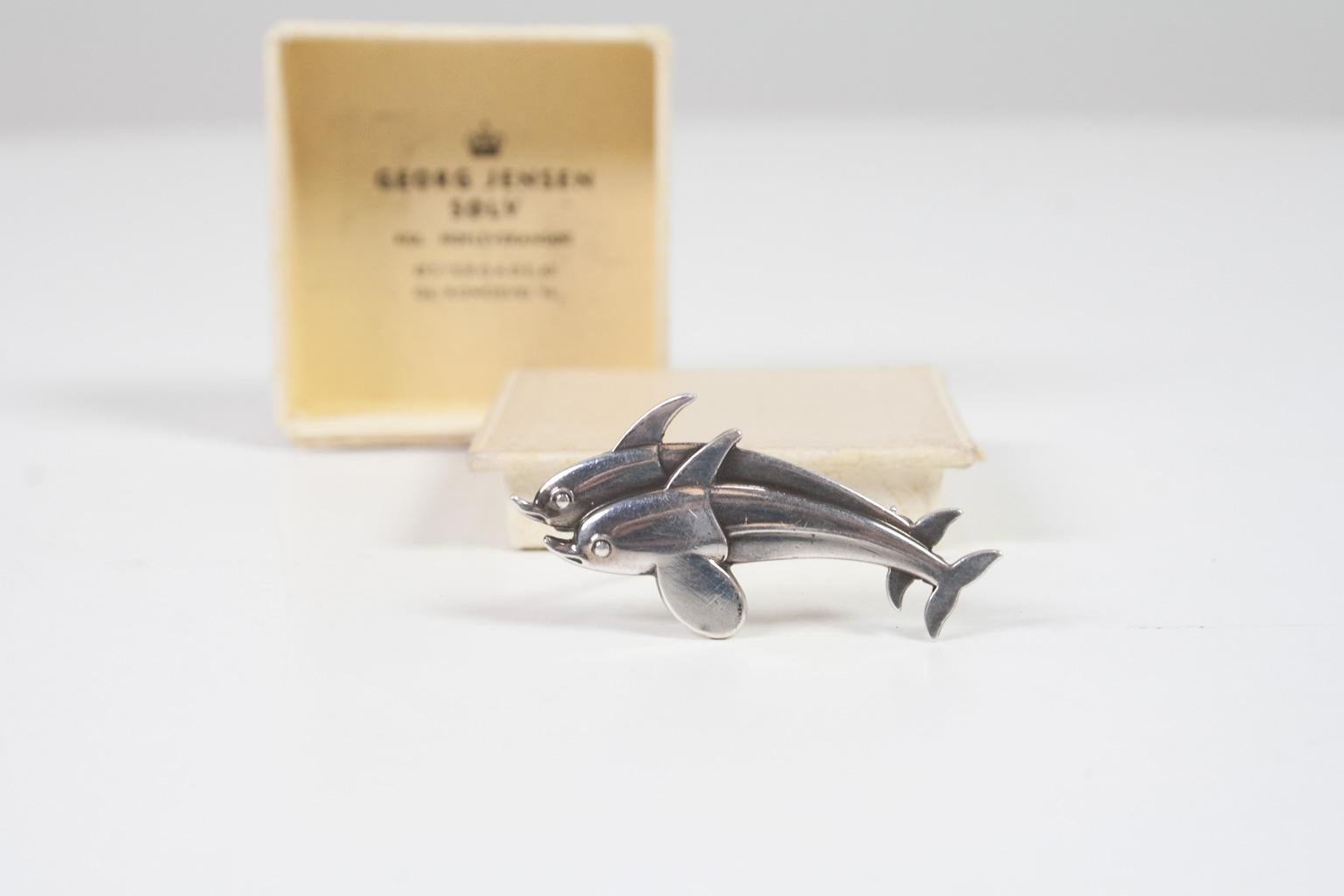 A cute vintage double dolphin brooch from George Jensen. This Scandinavian Modern sterling silver jewellery is designed by Harald Nielsen for George Jensen, with mark of George Jensen (after 1945). The brooch is in the original box. This vintage