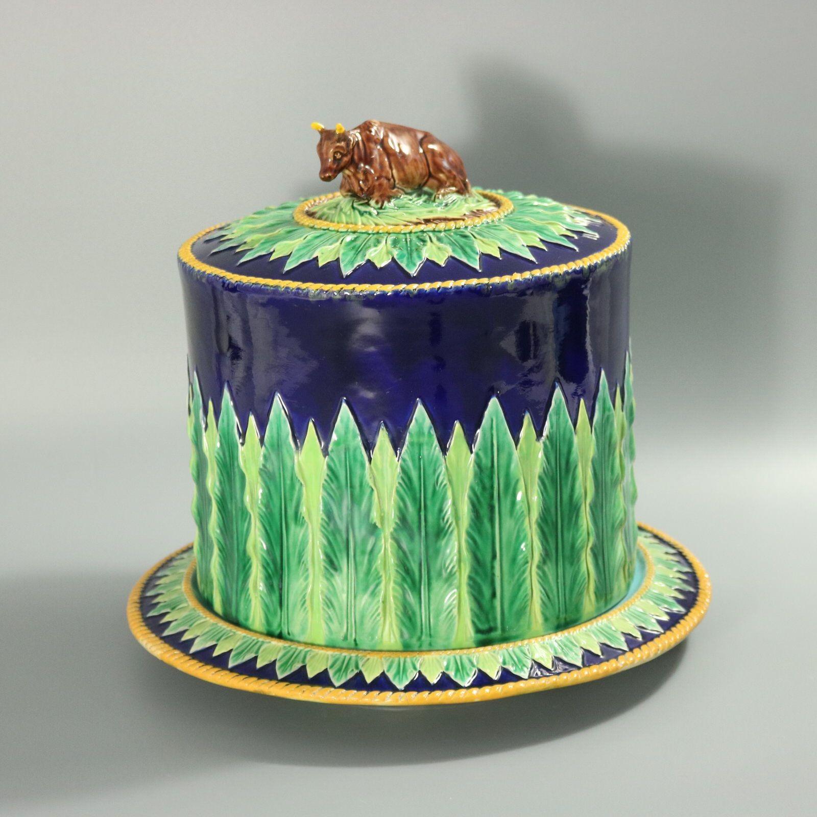 Garde-manger en majolique de George Jones représentant une vache couchée formant l'anse du couvercle et des bordures de feuilles rigides. Rare version à fond bleu cobalt. Coloration : le bleu de cobalt, le vert et le brun sont prédominants. La pièce