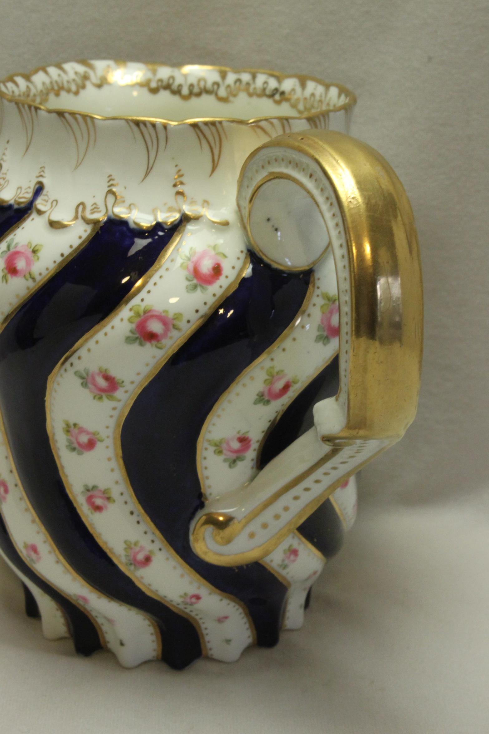 This very attractive, good quality porcelain hot water jug by George Jones & Co. is decorated with alternating flutes of hand painted roses and cobalt blue. It has then been finished off with delicate hand gilding. The shanked and gilded handle also