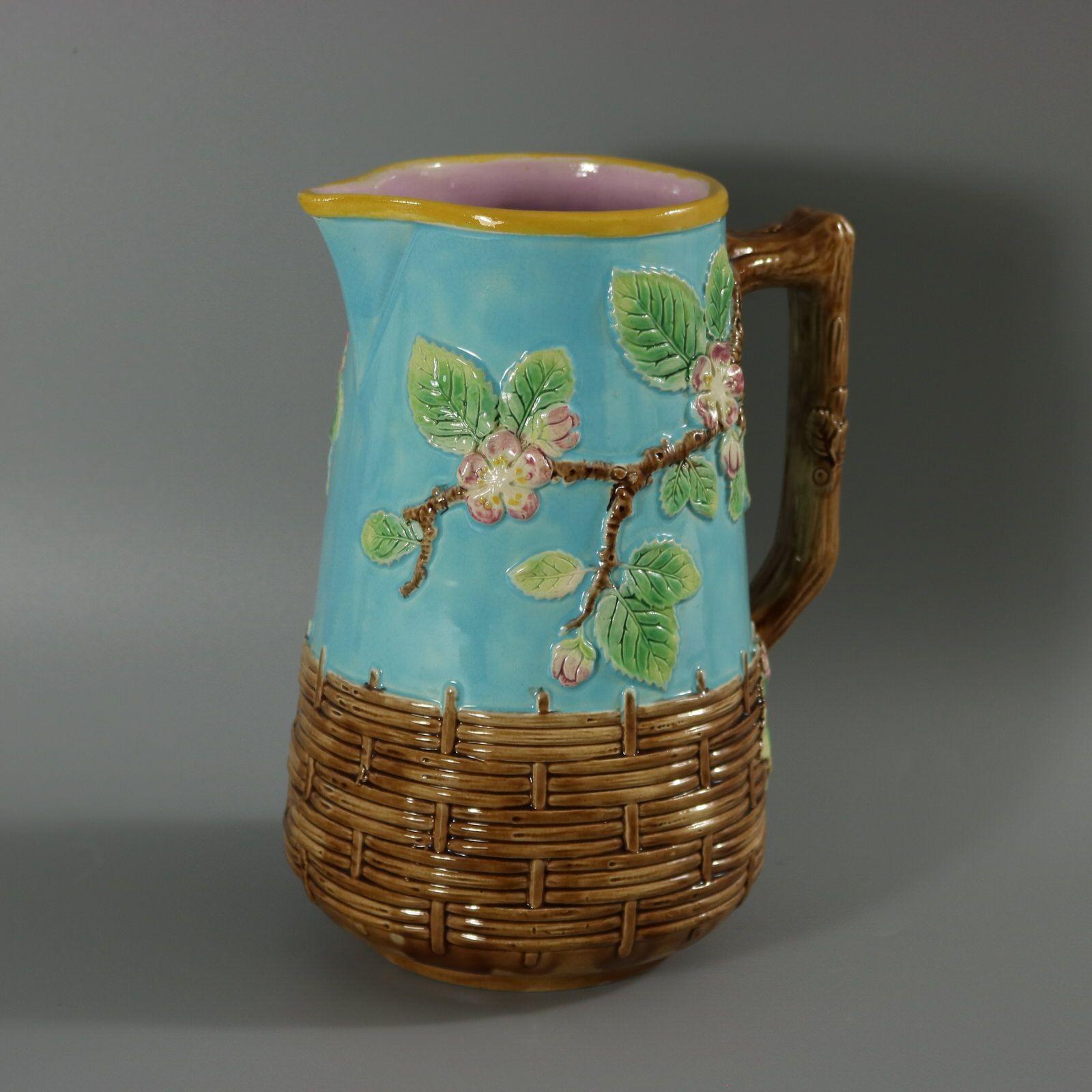 George Jones Majolica jug/pitcher which features a branch handle, with apple blossom branching off on either side and a basket weave border to bottom. Turquoise ground version. Colouration: turquoise, brown, green, are predominant. English diamond